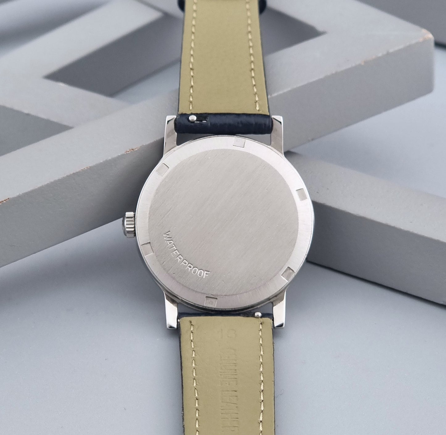 Vintage Omega Geneve 135.070 watch with a blue leather strap on a gray background case back view