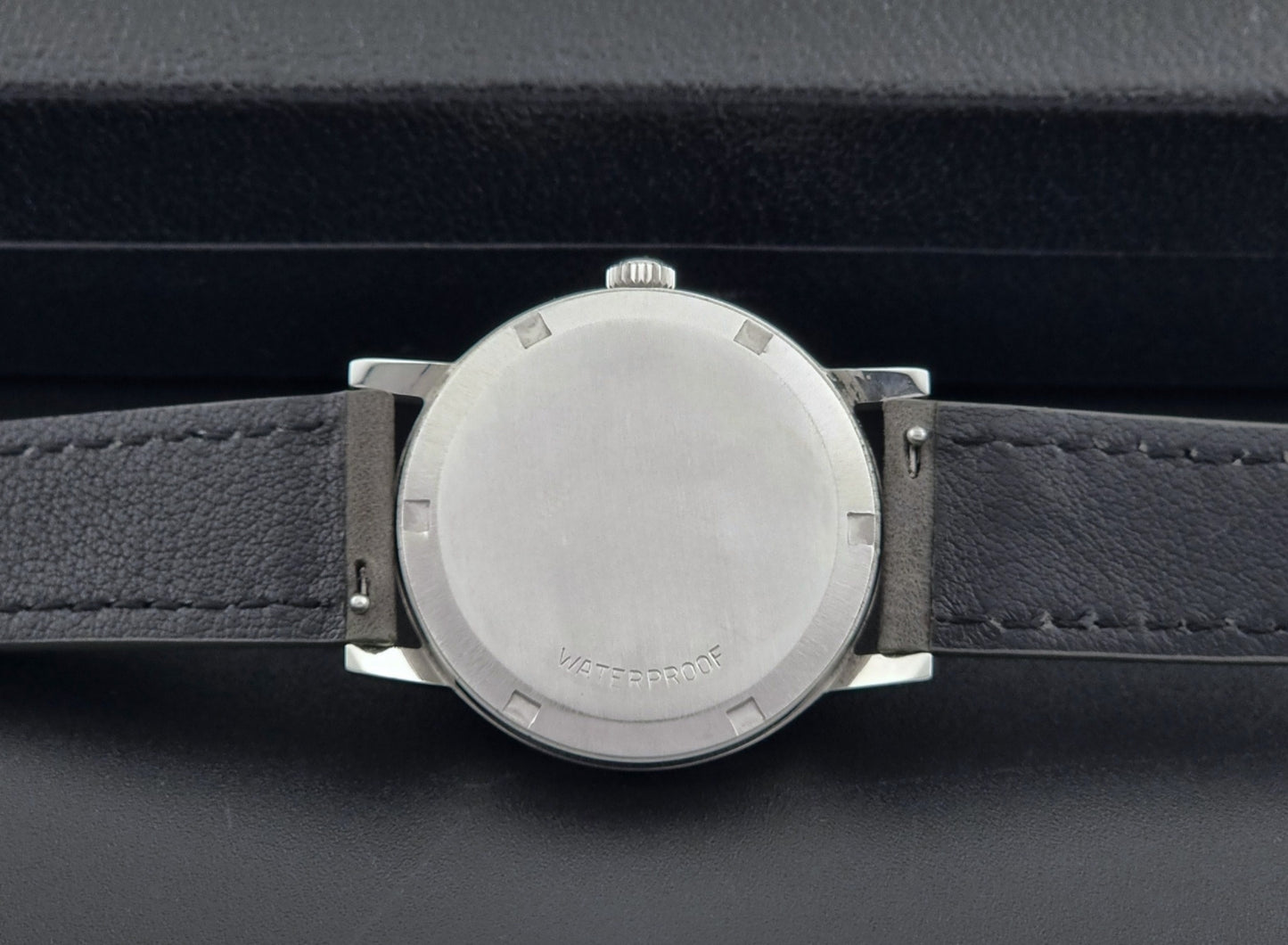 Vintage Omega watch Geneve 135.070 with grey leather strap on a dark surface case back view