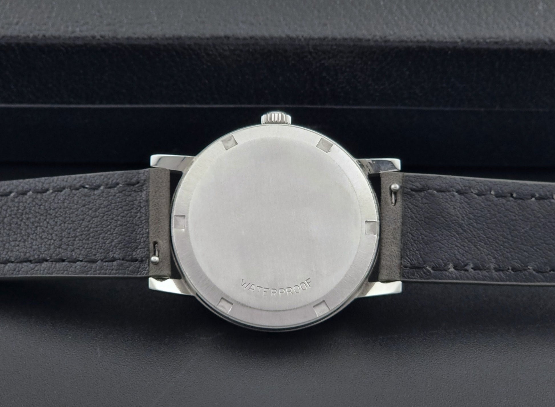 Vintage Omega watch Geneve 135.070 with grey leather strap on a dark surface case back view