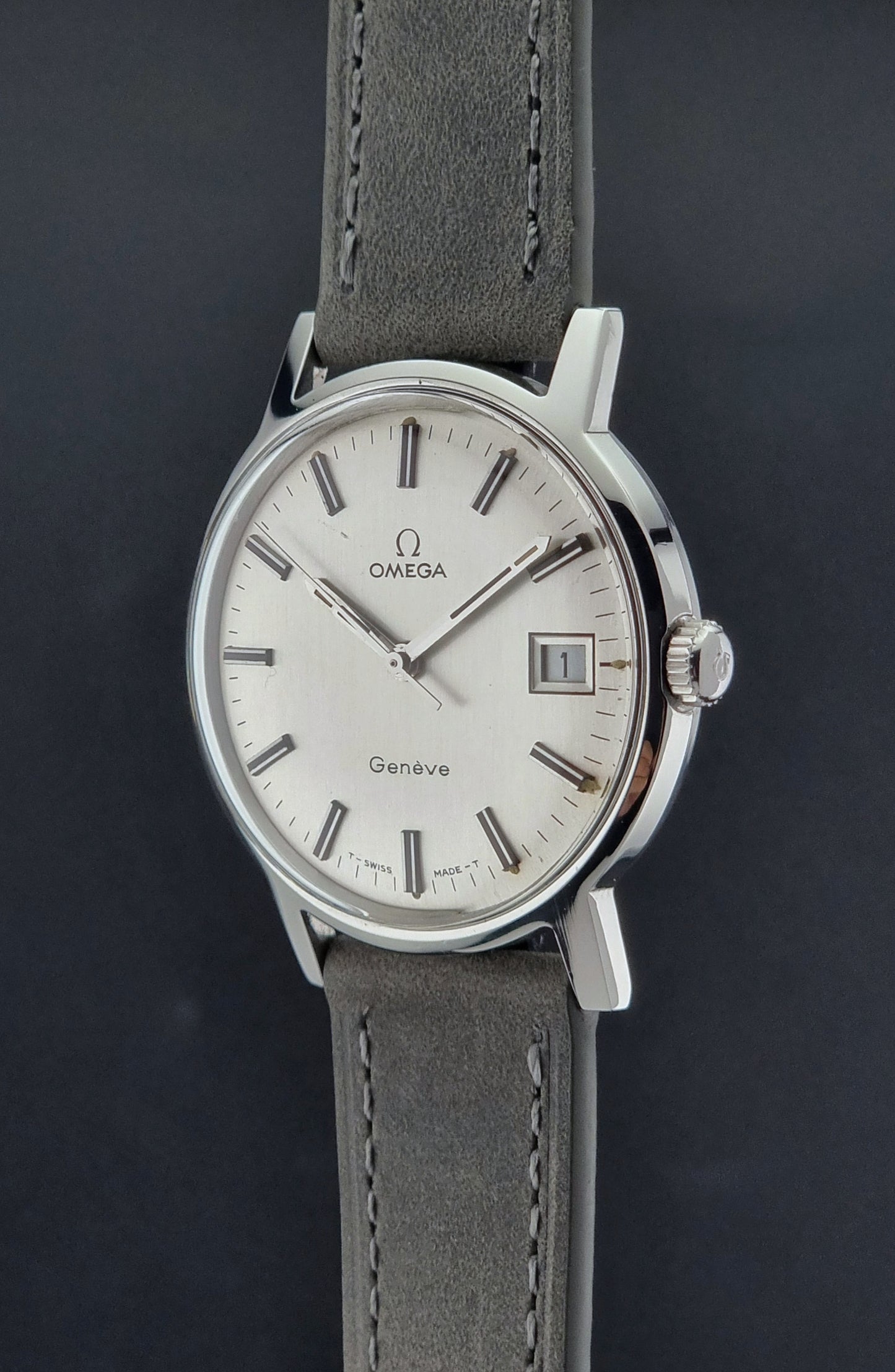 Vintage Omega watch Geneve 135.070 with grey leather strap on a dark surface crown profile view