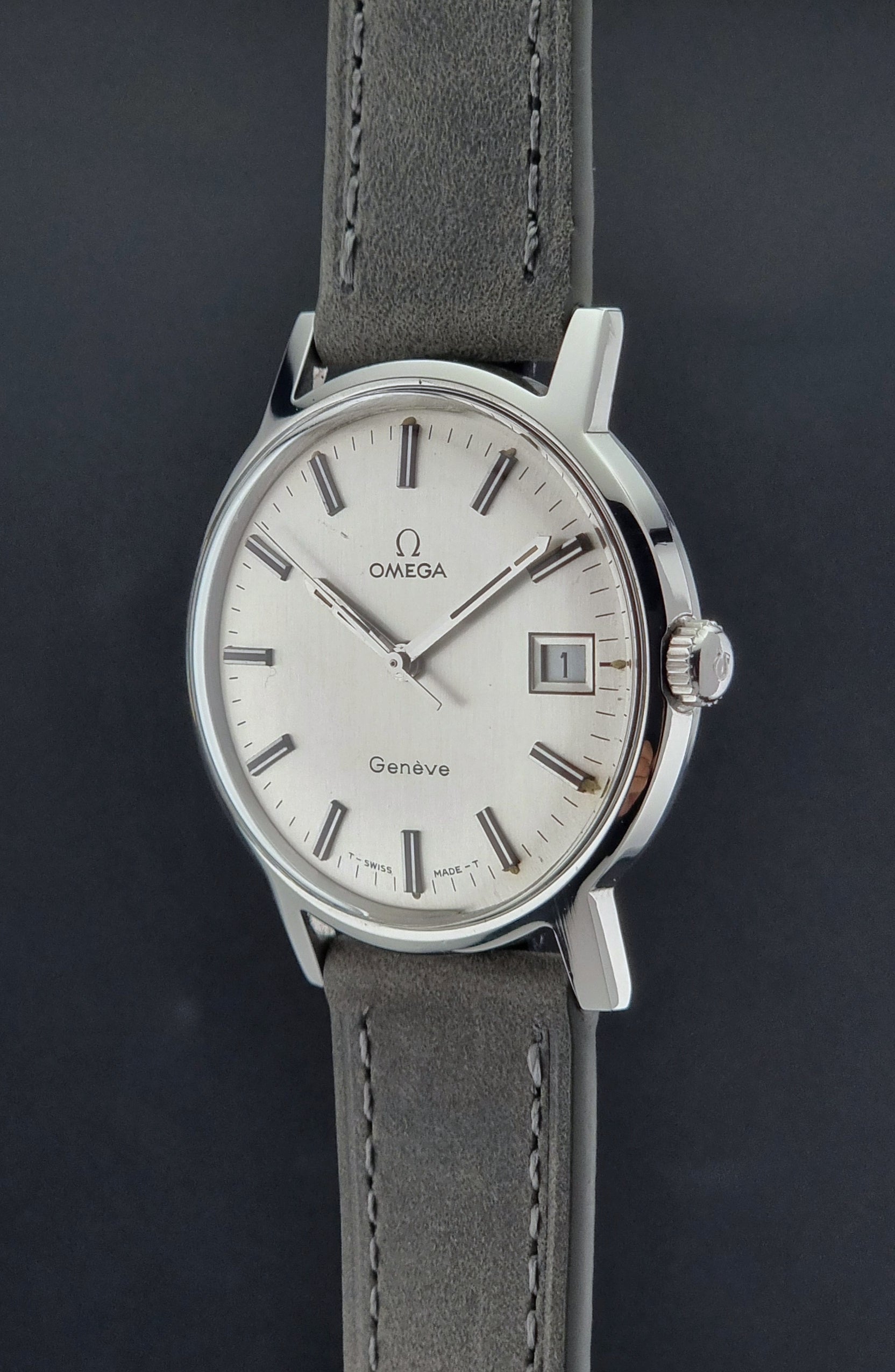 Vintage Omega watch Geneve 135.070 with grey leather strap on a dark surface crown profile view