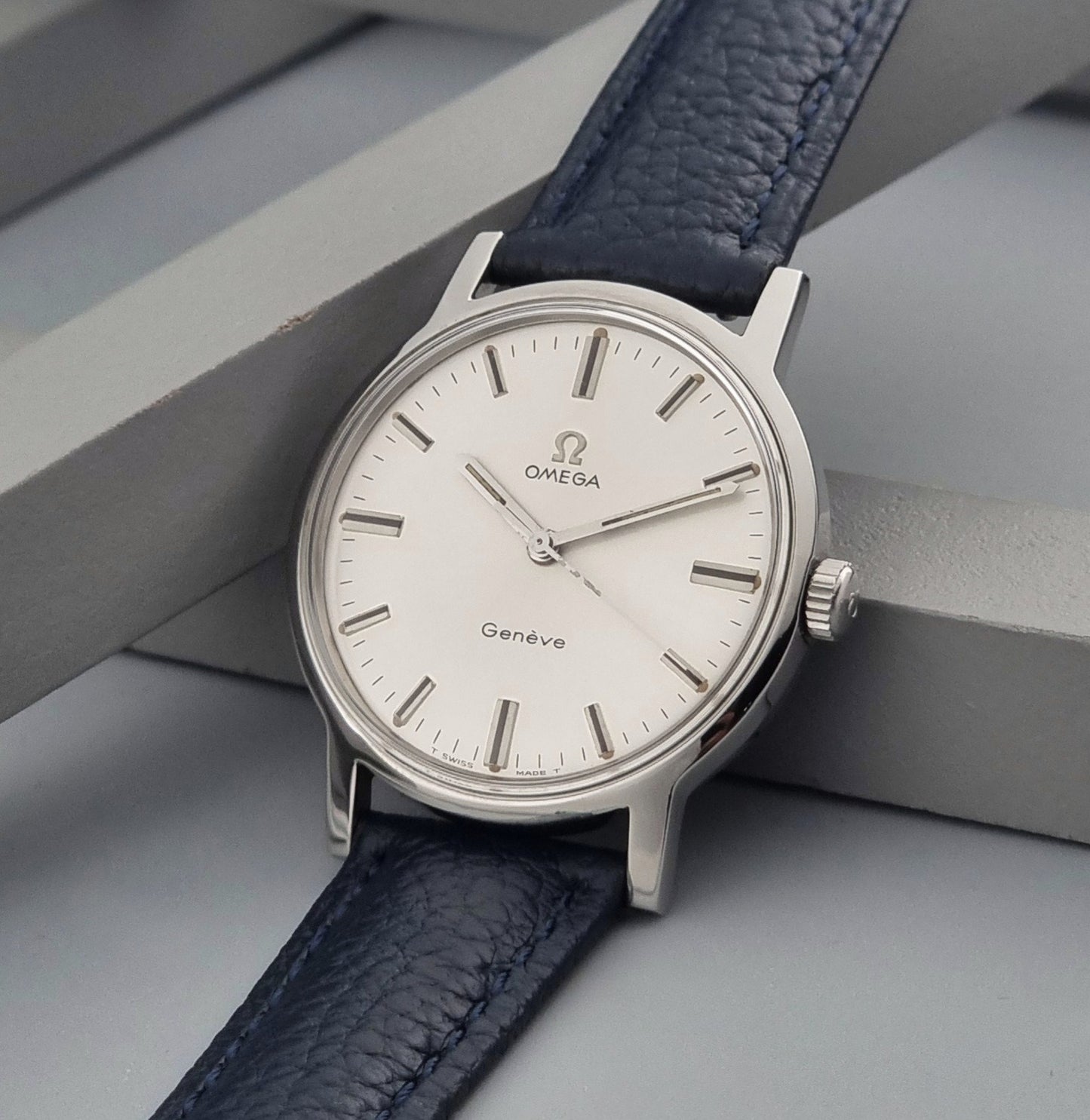 Vintage Omega Geneve 135.070 watch with a blue leather strap on a gray background crown view