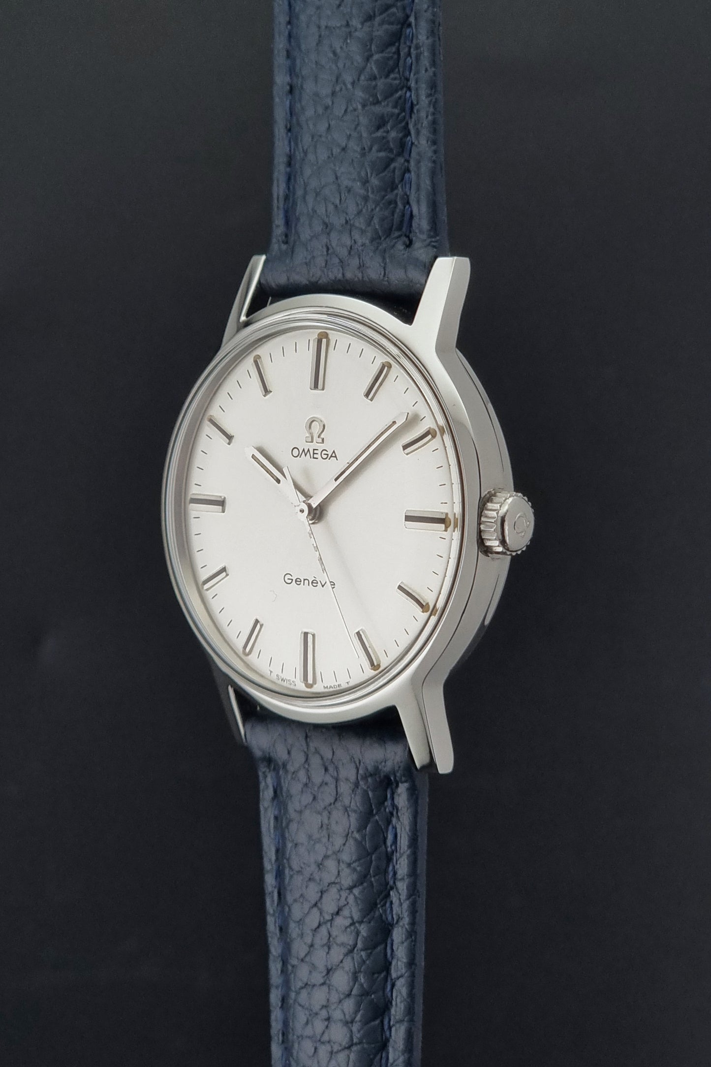 Vintage Omega Geneve 135.070 watch with a blue leather strap on a gray background crown profile view