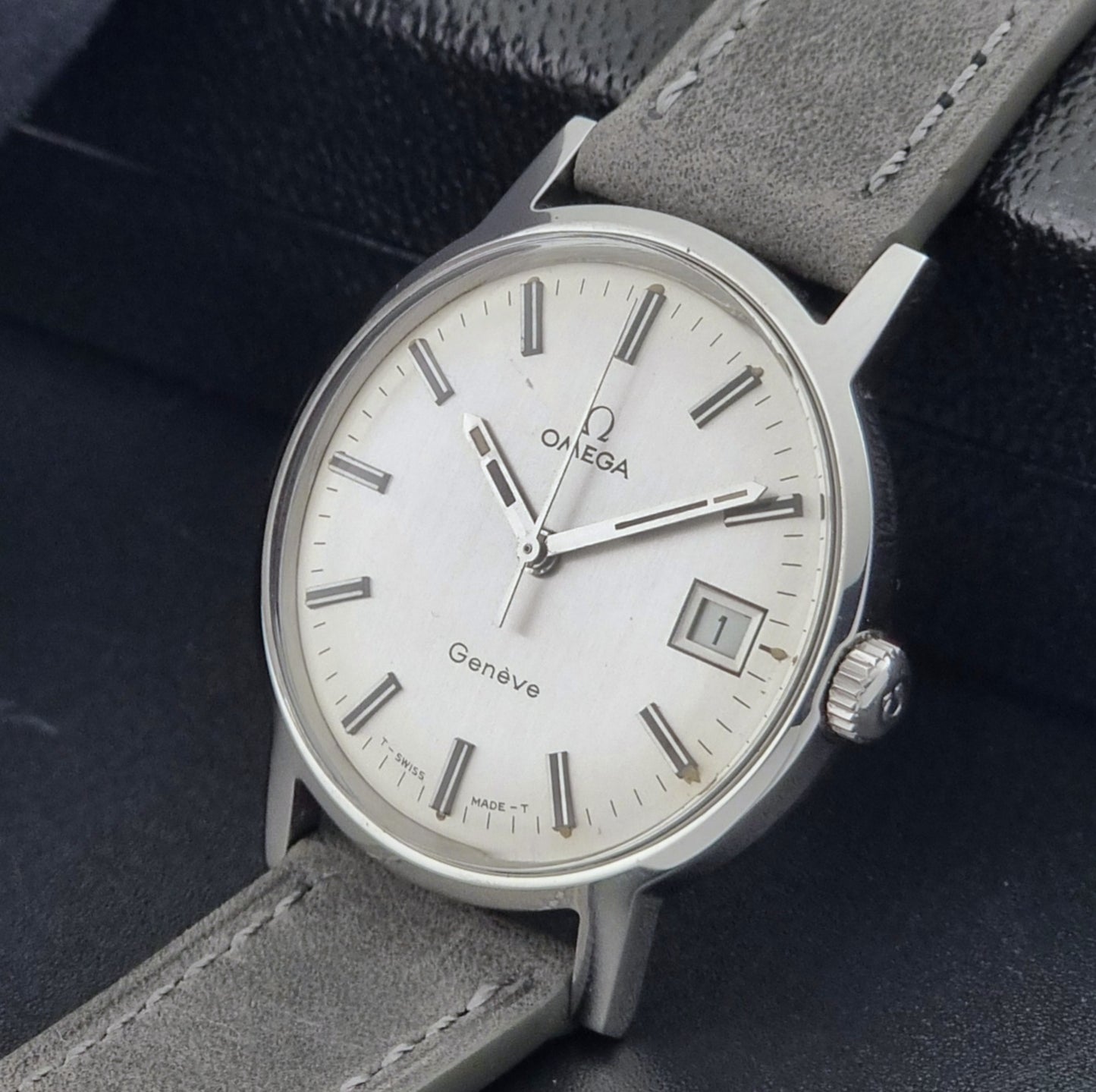 Vintage Omega watch Geneve 135.070 with grey leather strap on a dark surface crown view