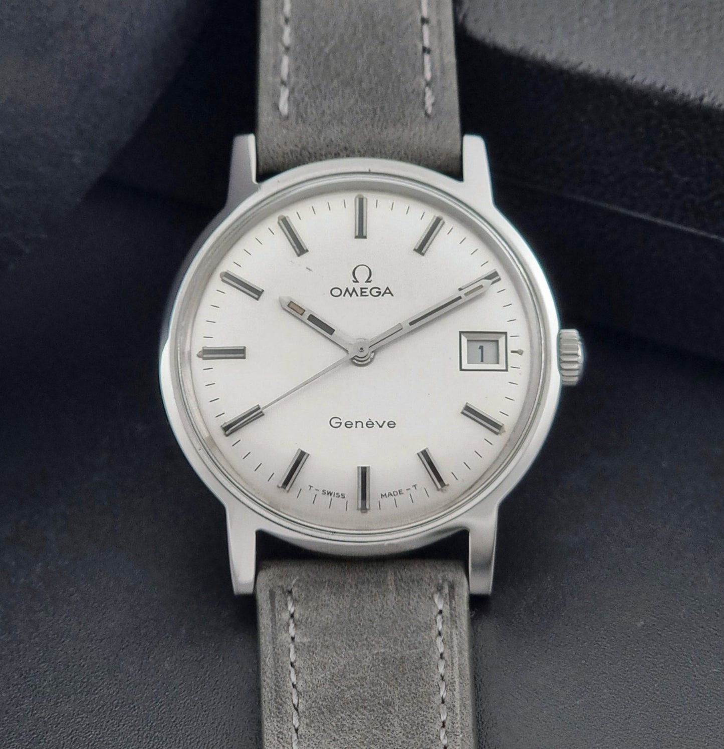 Vintage Omega watch Geneve 135.070 with grey leather strap on a dark surface close dial view