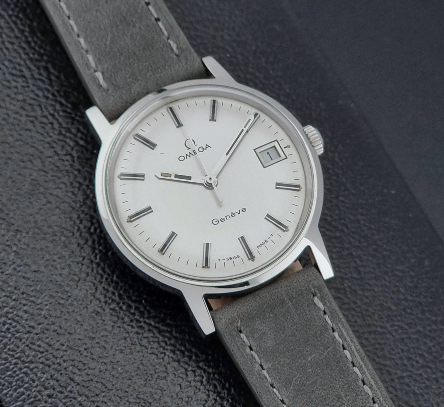 Vintage Omega watch Geneve 135.070 with grey leather strap on a dark surface dial view