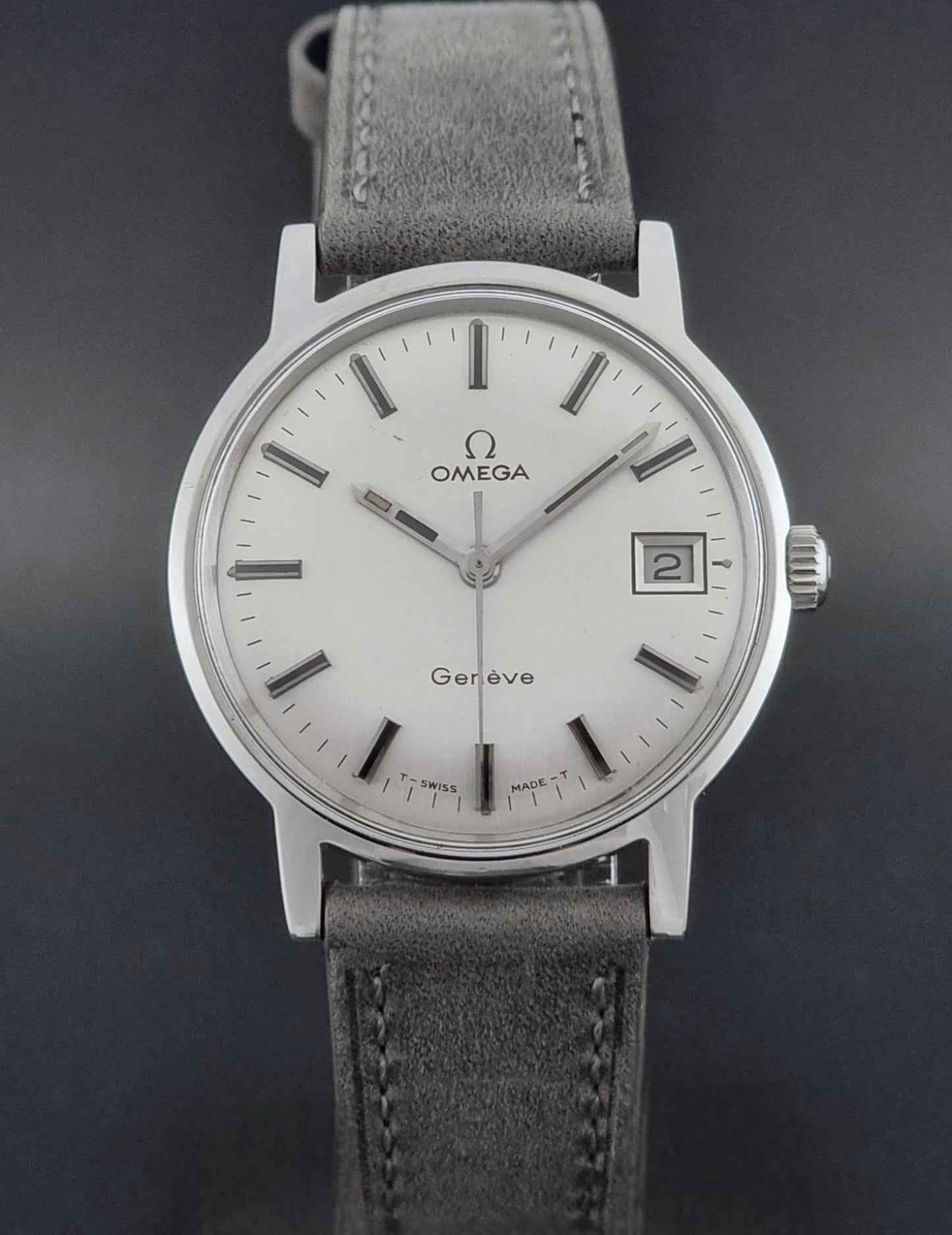 Vintage Omega watch Geneve 135.070 with grey leather strap on a dark surface close front view