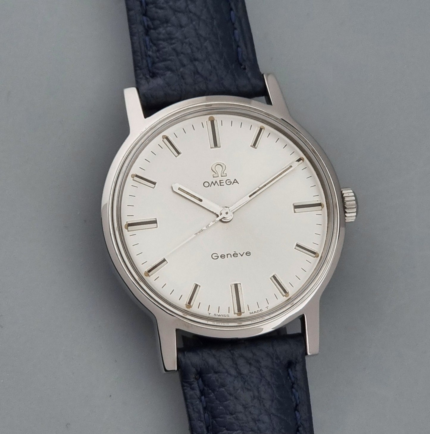 Vintage Omega Geneve 135.070 watch with a blue leather strap on a gray background front view
