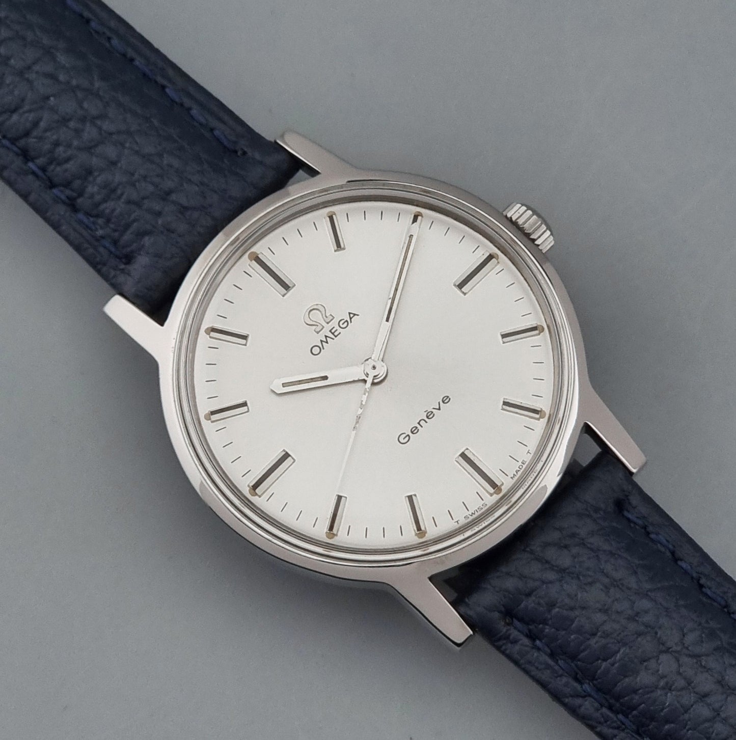 Vintage Omega Geneve 135.070 watch with a blue leather strap on a gray background close dial view