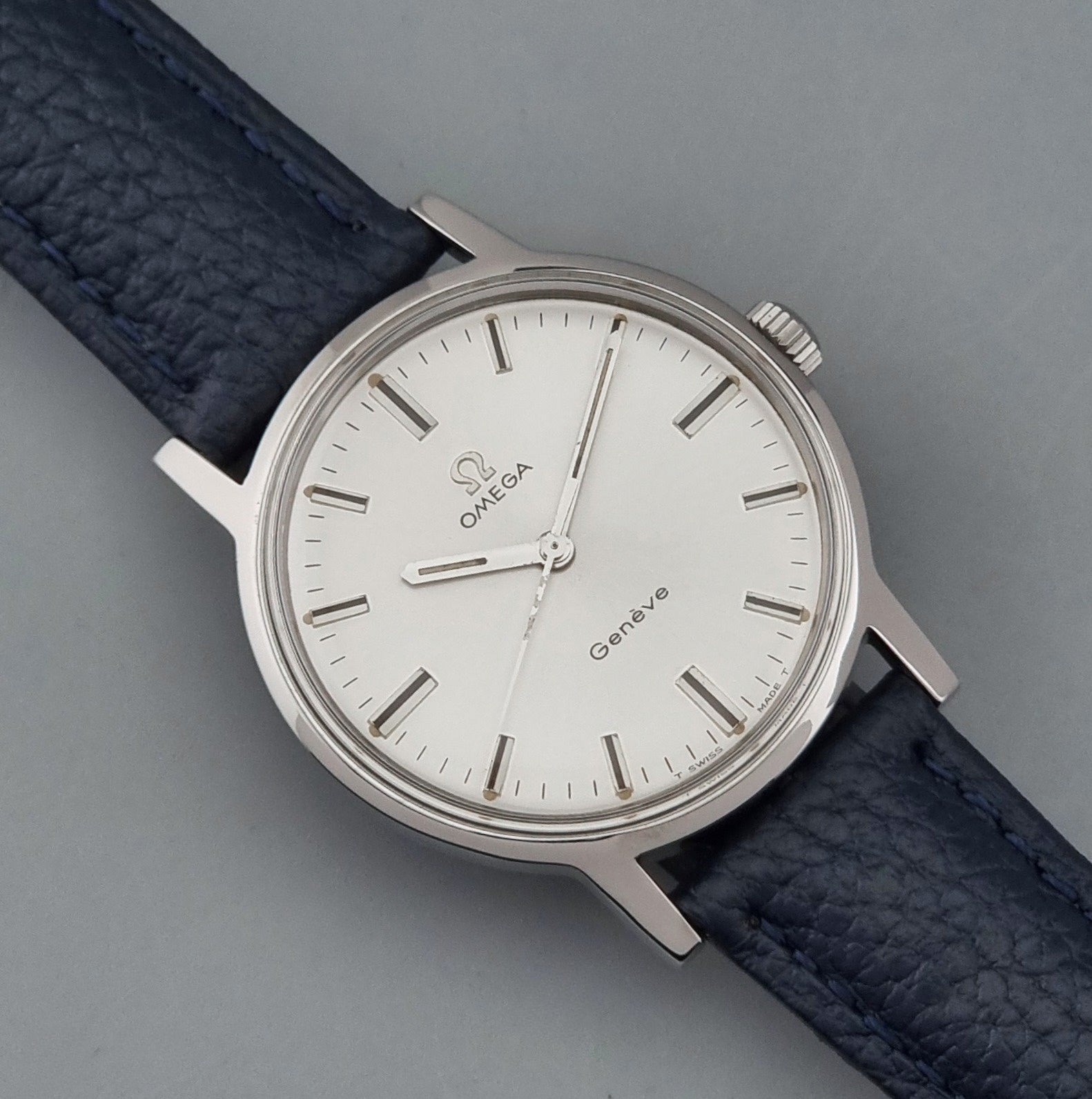Vintage Omega Geneve 135.070 watch with a blue leather strap on a gray background close dial view