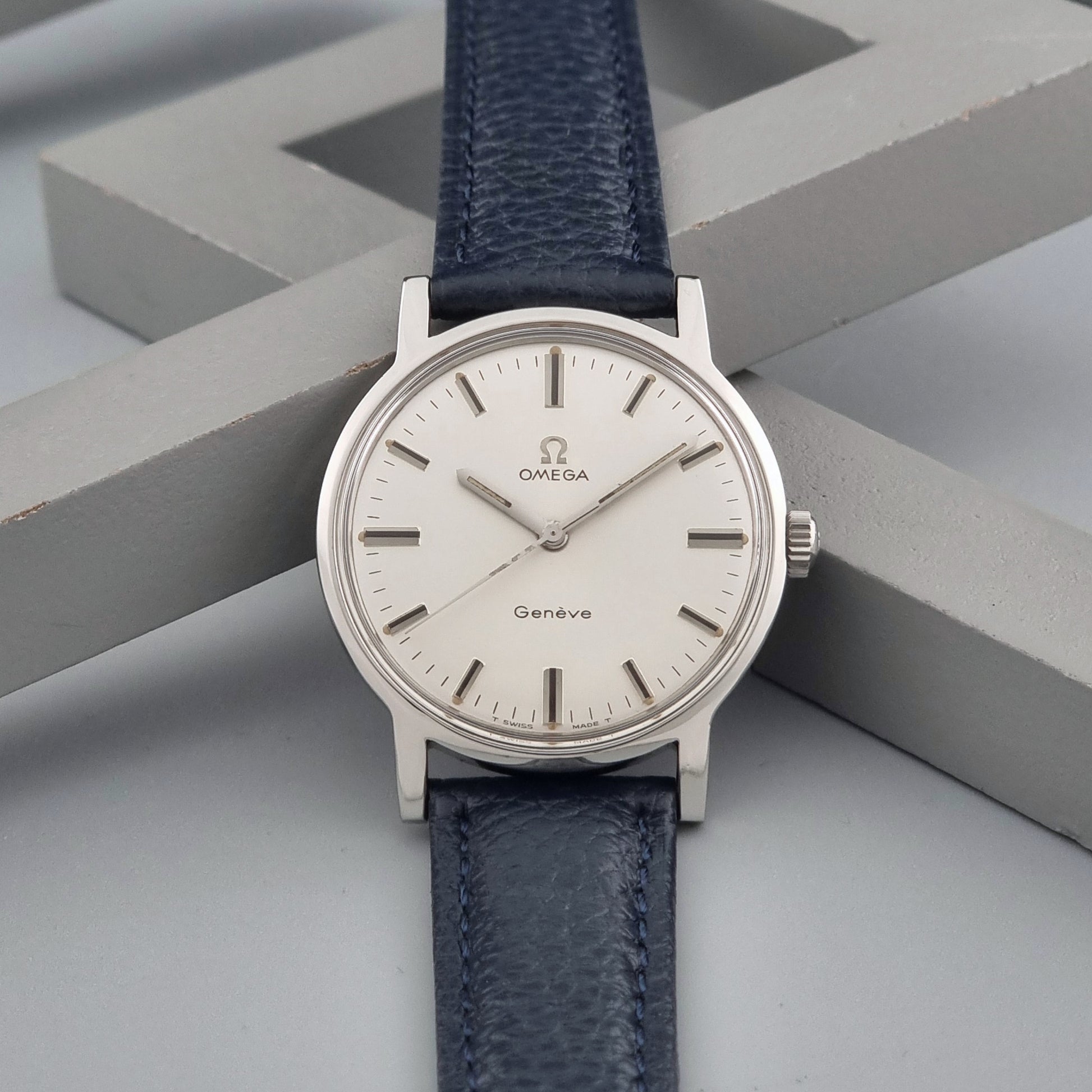 Vintage Omega Geneve 135.070 watch with a blue leather strap on a gray background dial view