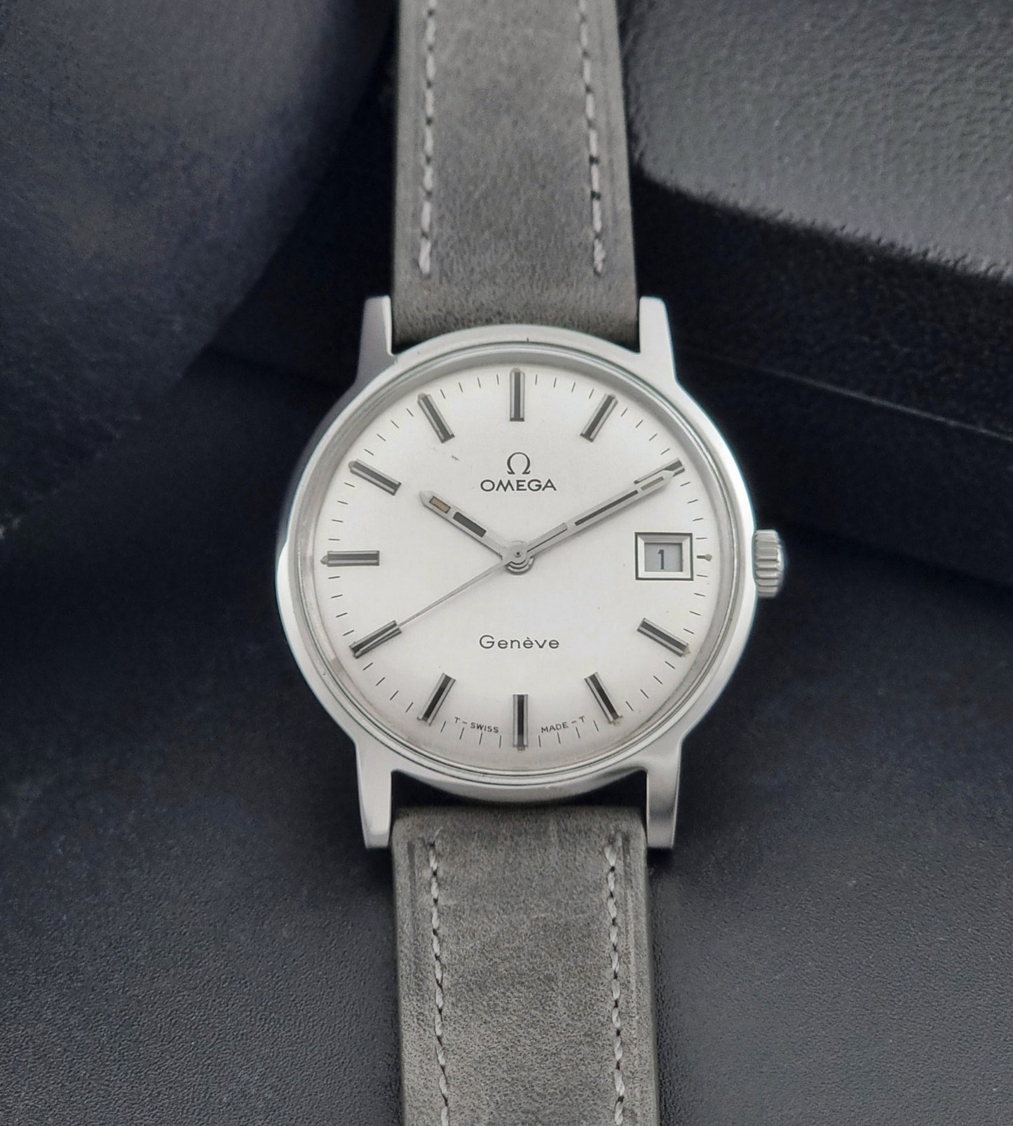 Vintage Omega watch Geneve 135.070 with grey leather strap on a dark surface front view