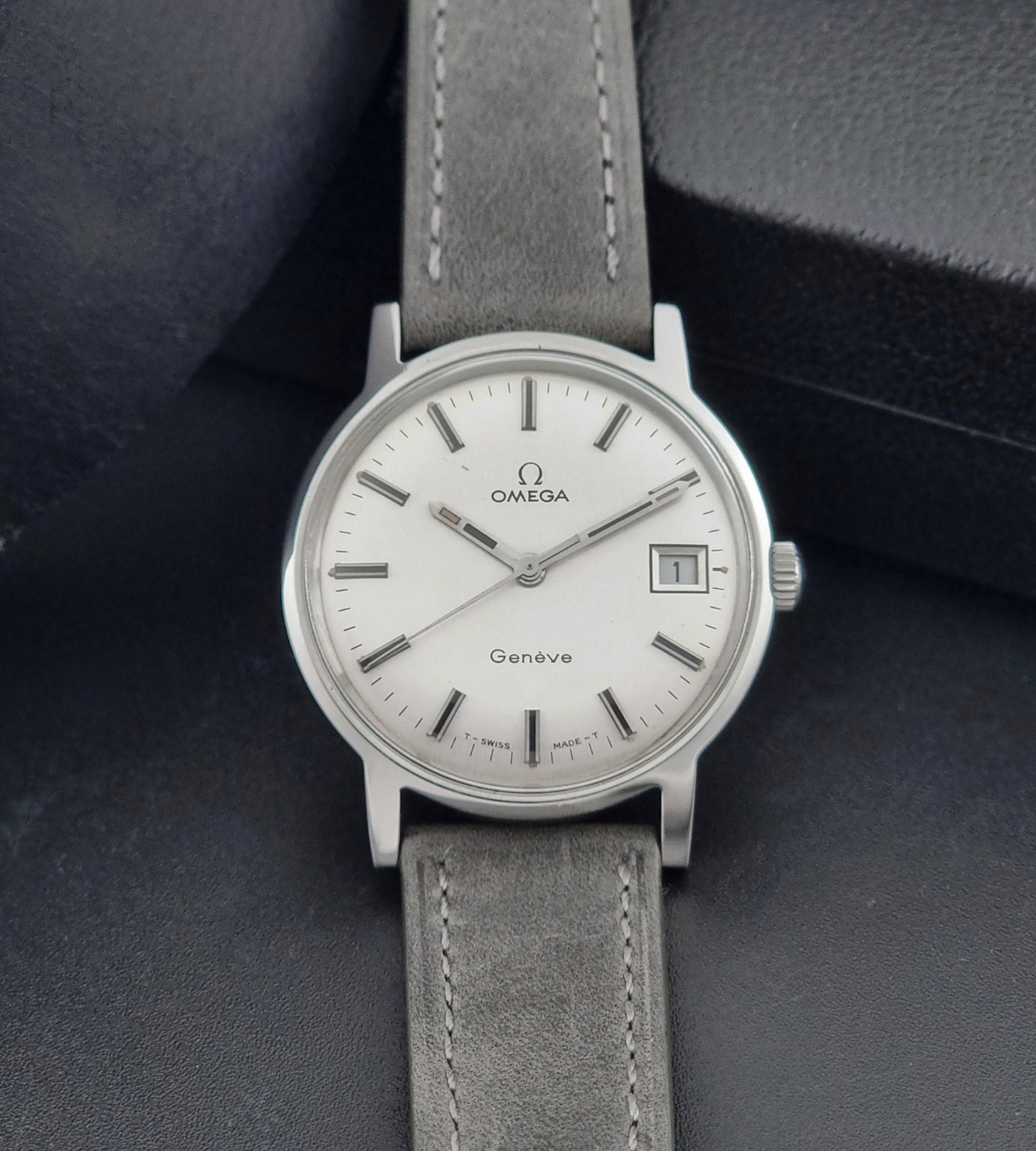 Vintage Omega watch Geneve 135.070 with grey leather strap on a dark surface front view