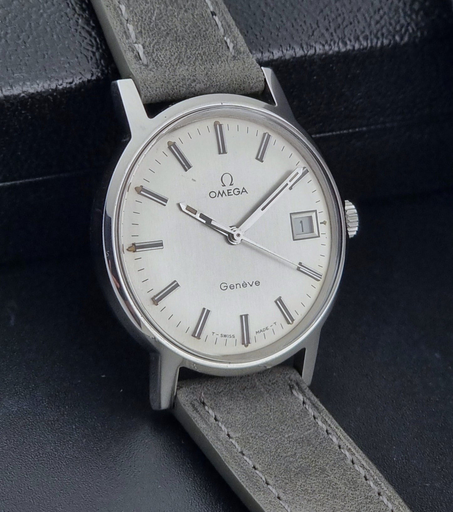 Vintage Omega watch Geneve 135.070 with grey leather strap on a dark surface side view