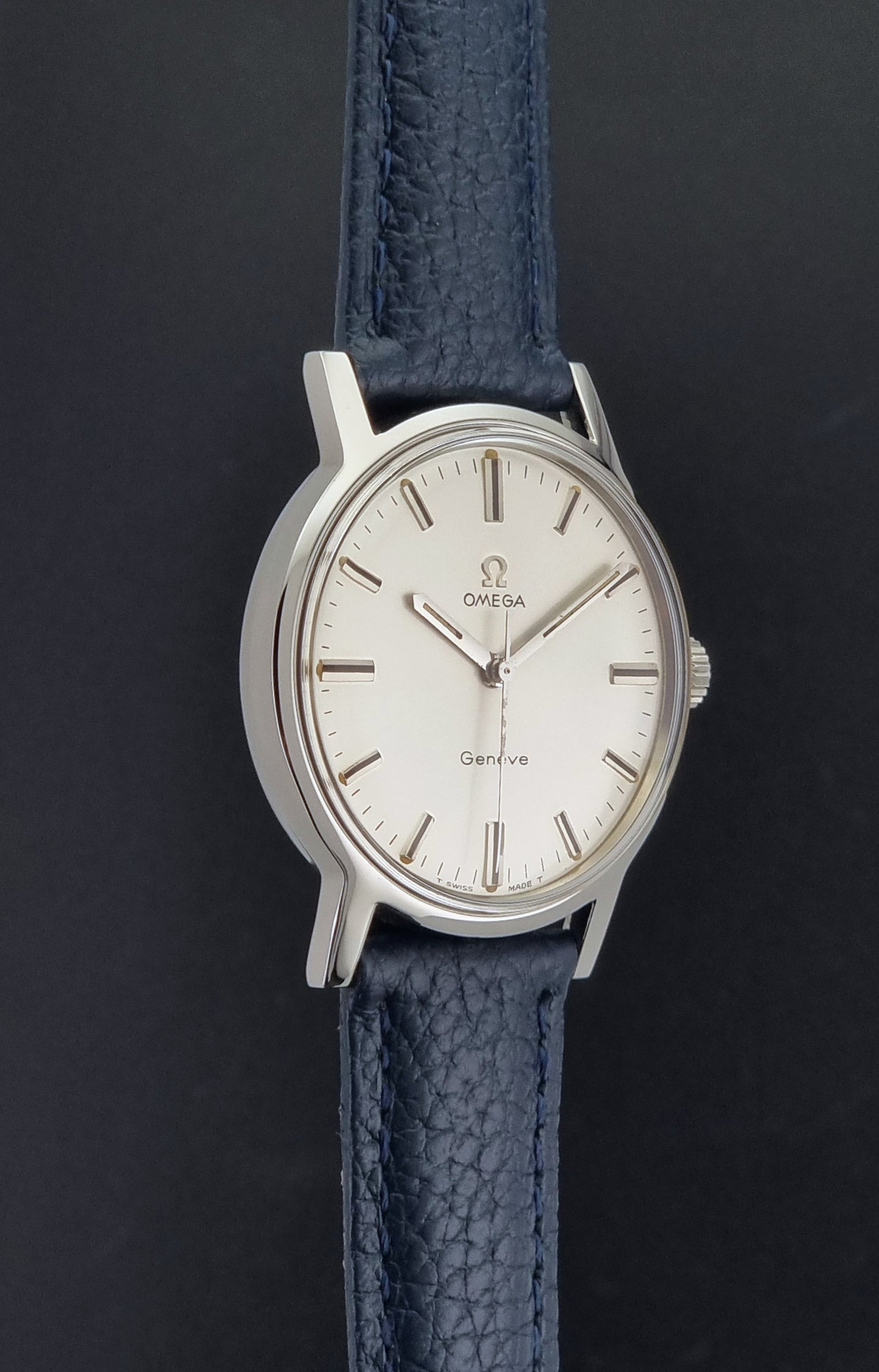 Vintage Omega Geneve 135.070 watch with a blue leather strap on a gray background side profile view