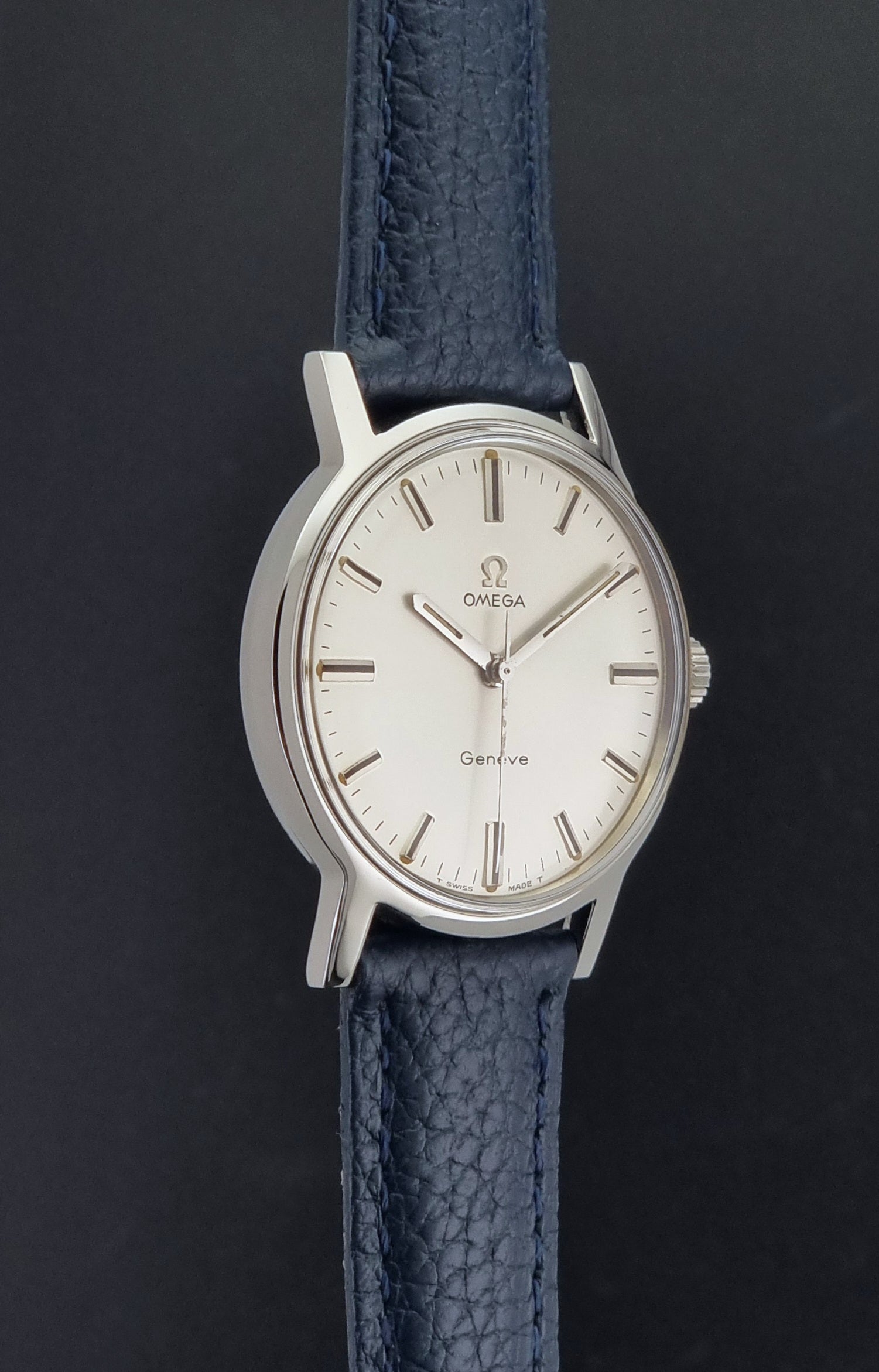 Vintage Omega Geneve 135.070 watch with a blue leather strap on a gray background side profile view