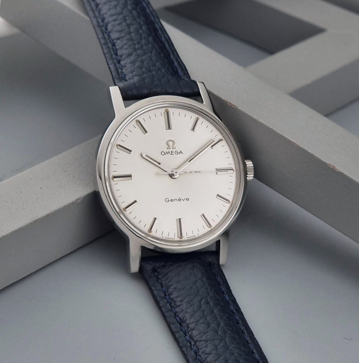Vintage Omega Geneve 135.070 watch with a blue leather strap on a gray background side view