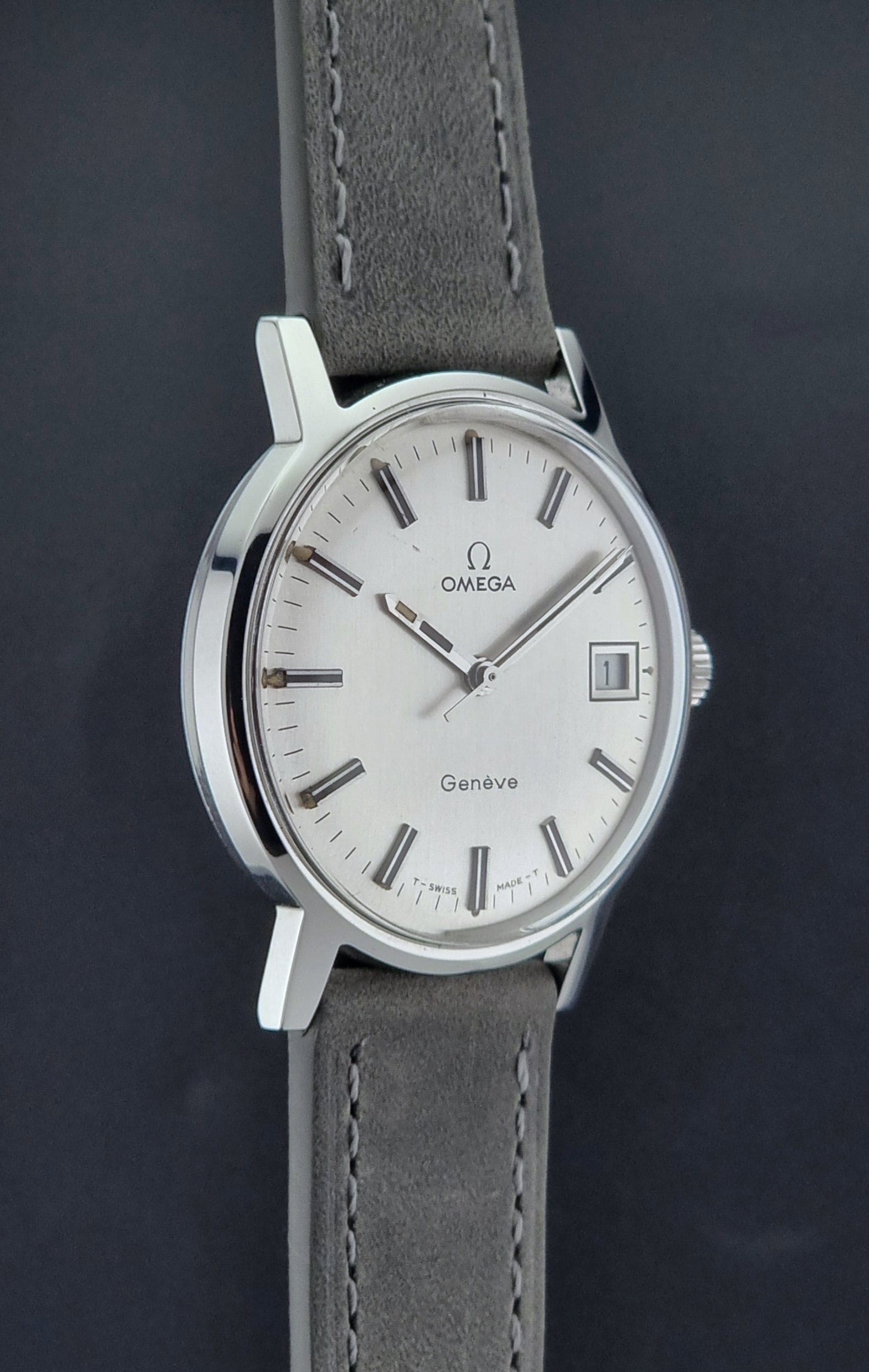 Vintage Omega watch Geneve 135.070 with grey leather strap on a dark surface side profile view