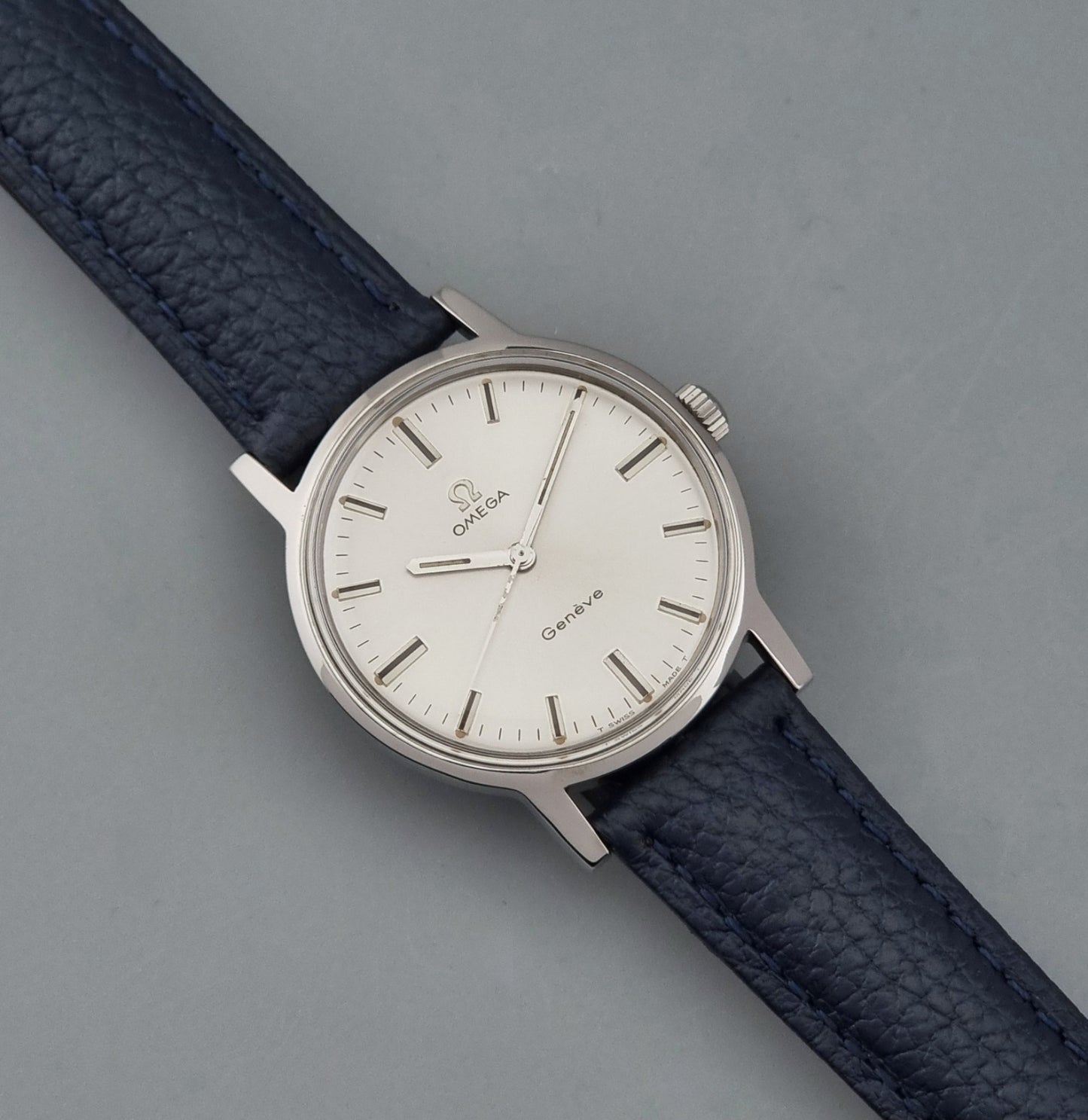 Vintage Omega Geneve 135.070 watch with a blue leather strap on a gray background dial