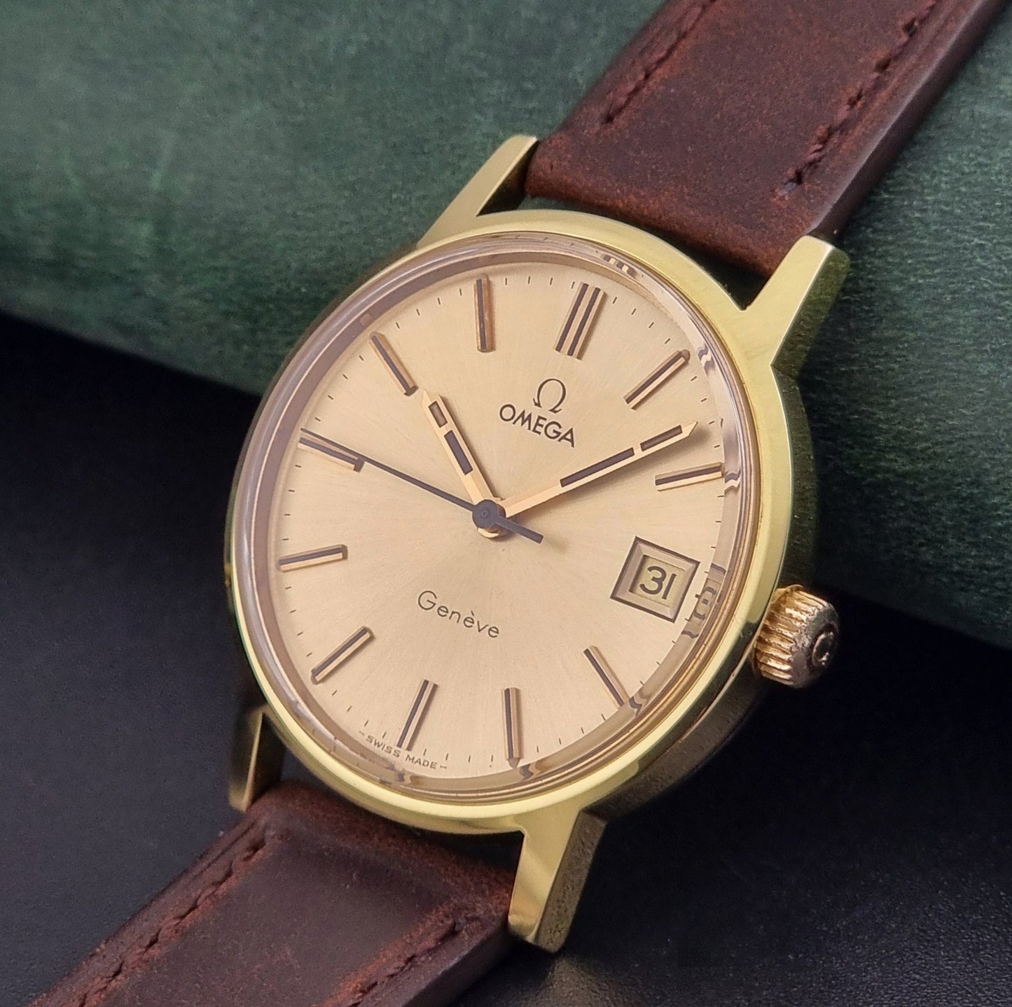 Vintage Omega Wristwatch Geneve 136.0098 with brown leather strap on a green surface crown view