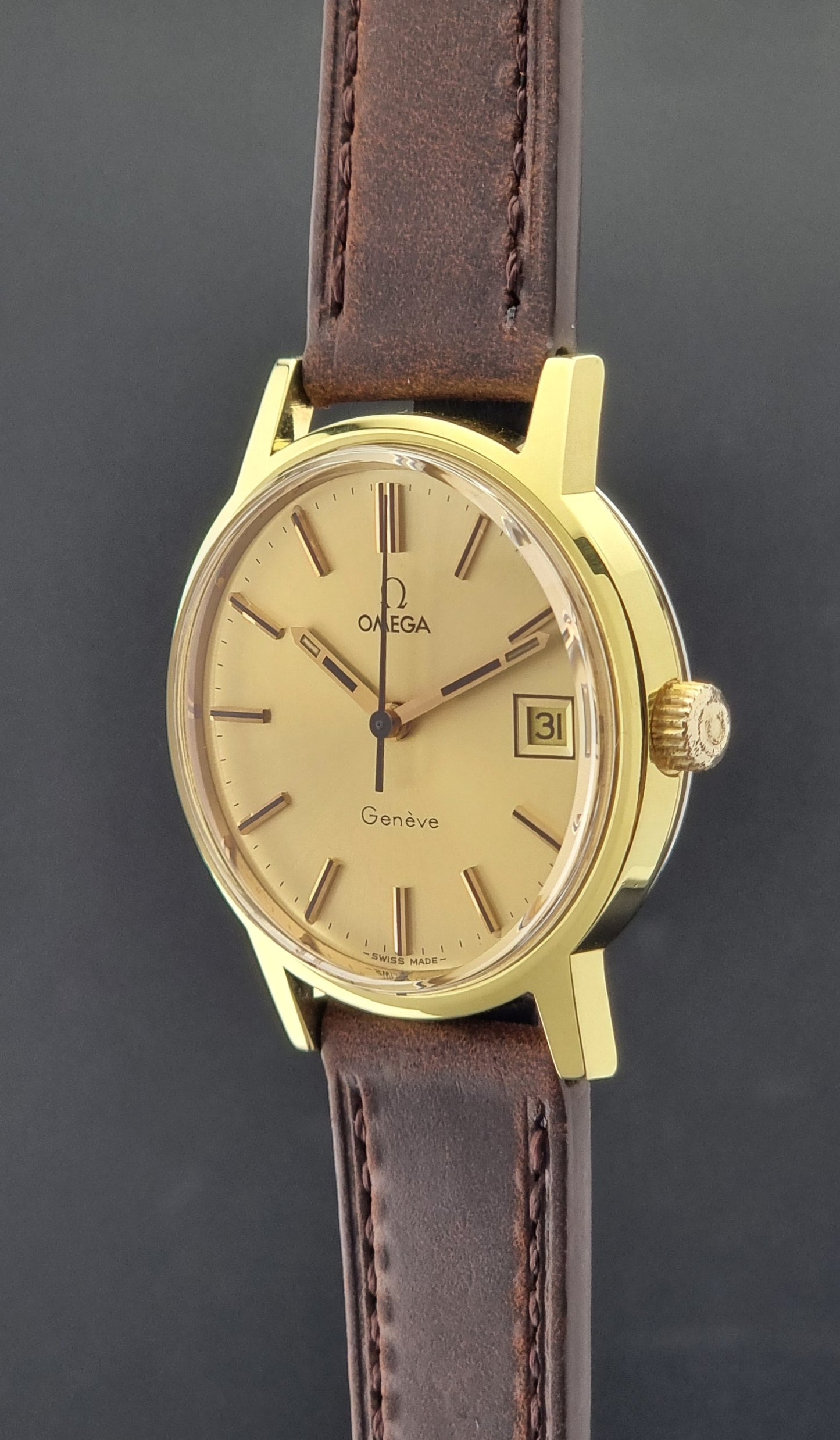Vintage Omega Wristwatch Geneve 136.0098 with brown leather strap on a green surface crown profile view