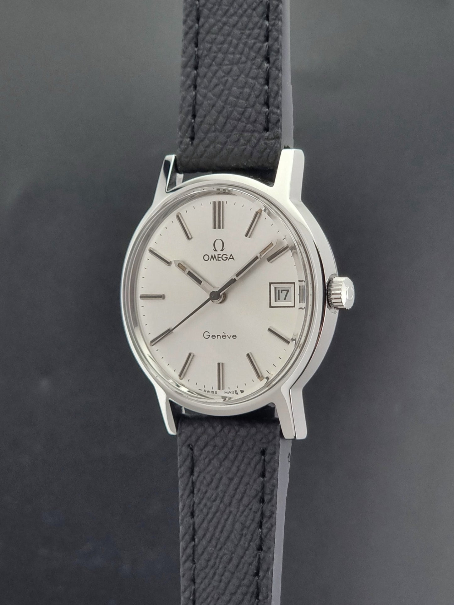 Vintage Omega Geneve 136.0098 Wristwatch with black strap and silver case on a gray background crown profile view