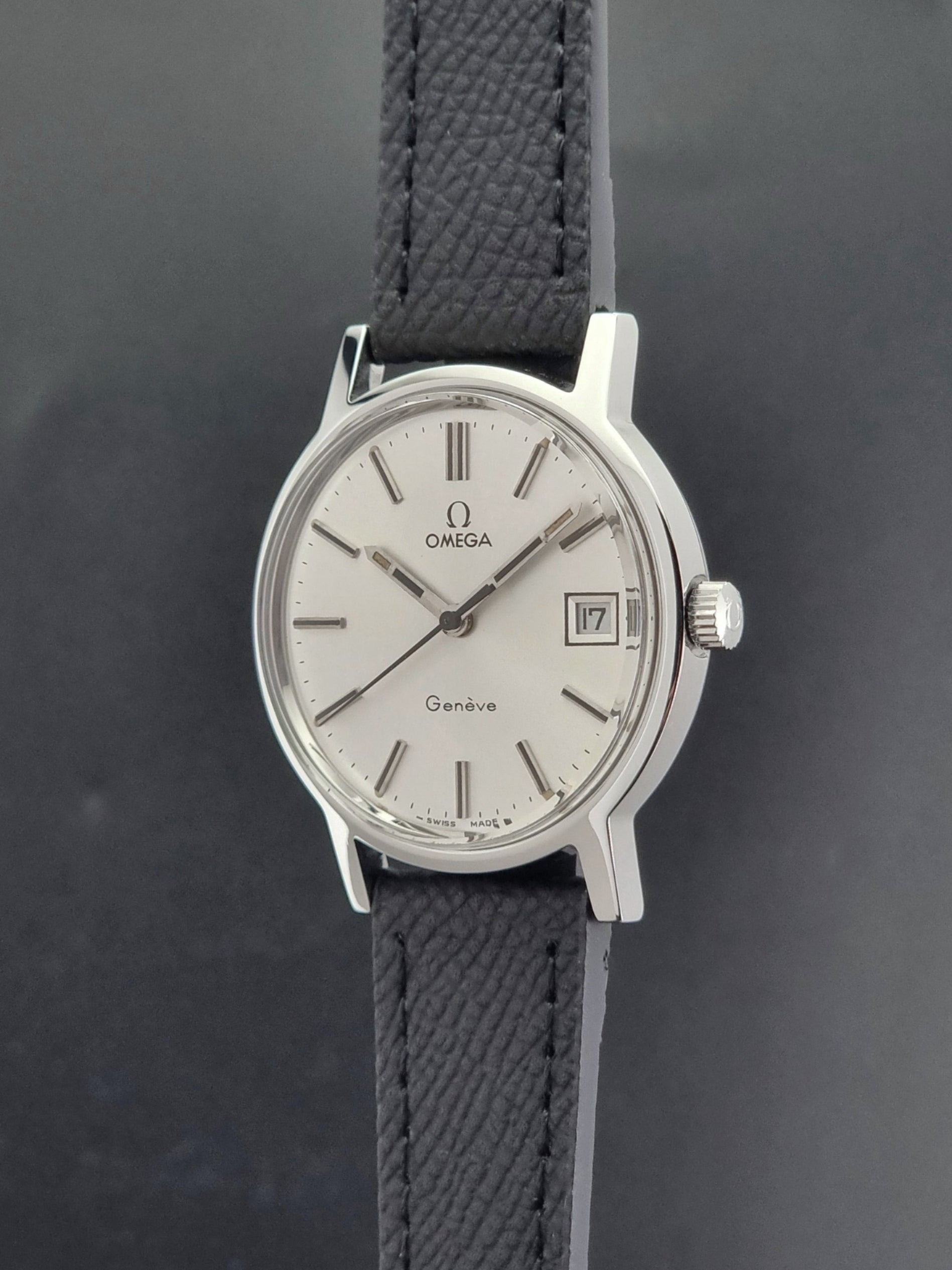 Vintage Omega Geneve 136.0098 Wristwatch with black strap and silver case on a gray background crown profile view