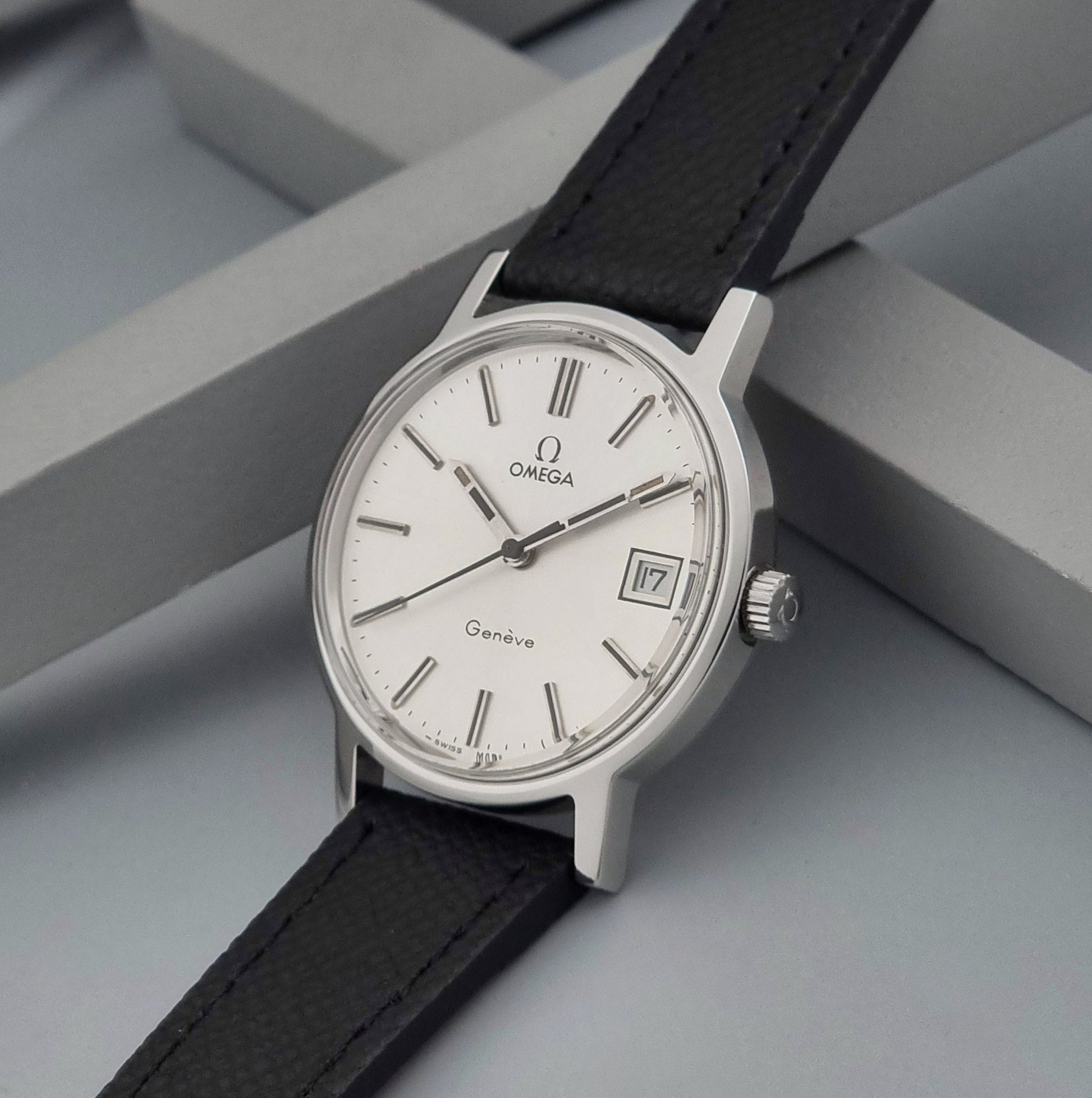 Vintage Omega Geneve 136.0098 Wristwatch with black strap and silver case on a gray background crown view