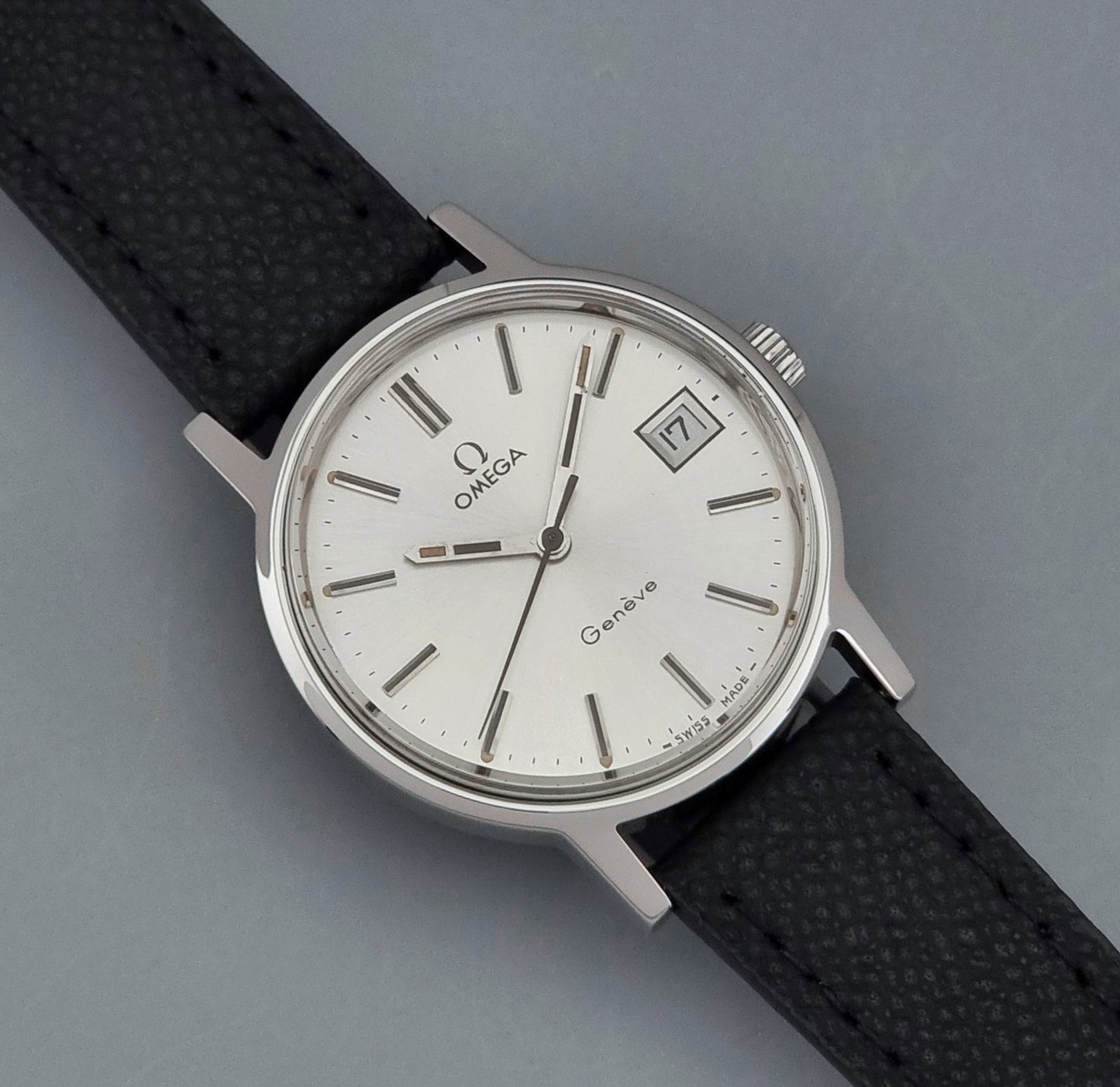 Vintage Omega Geneve 136.0098 Wristwatch with black strap and silver case on a gray background close up dial view