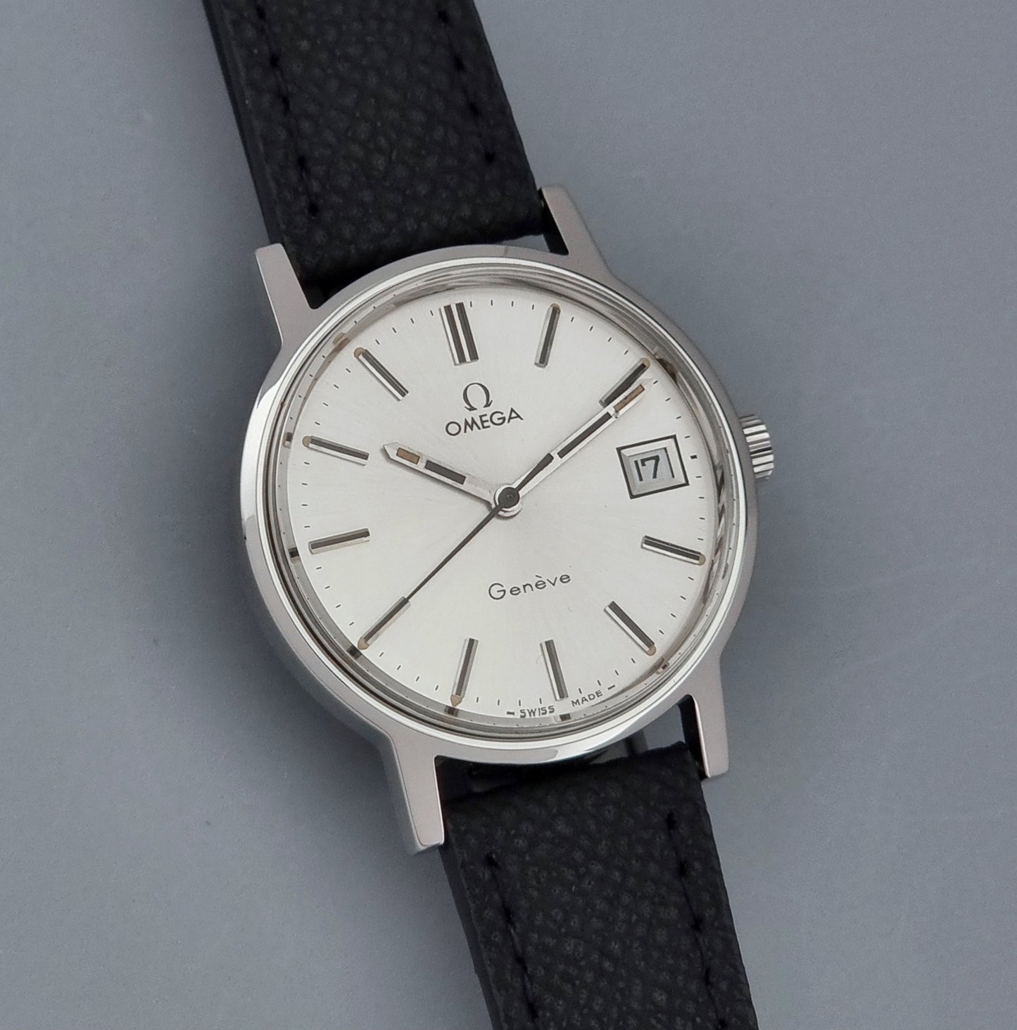 Vintage Omega Geneve 136.0098 Wristwatch with black strap and silver case on a gray background front view
