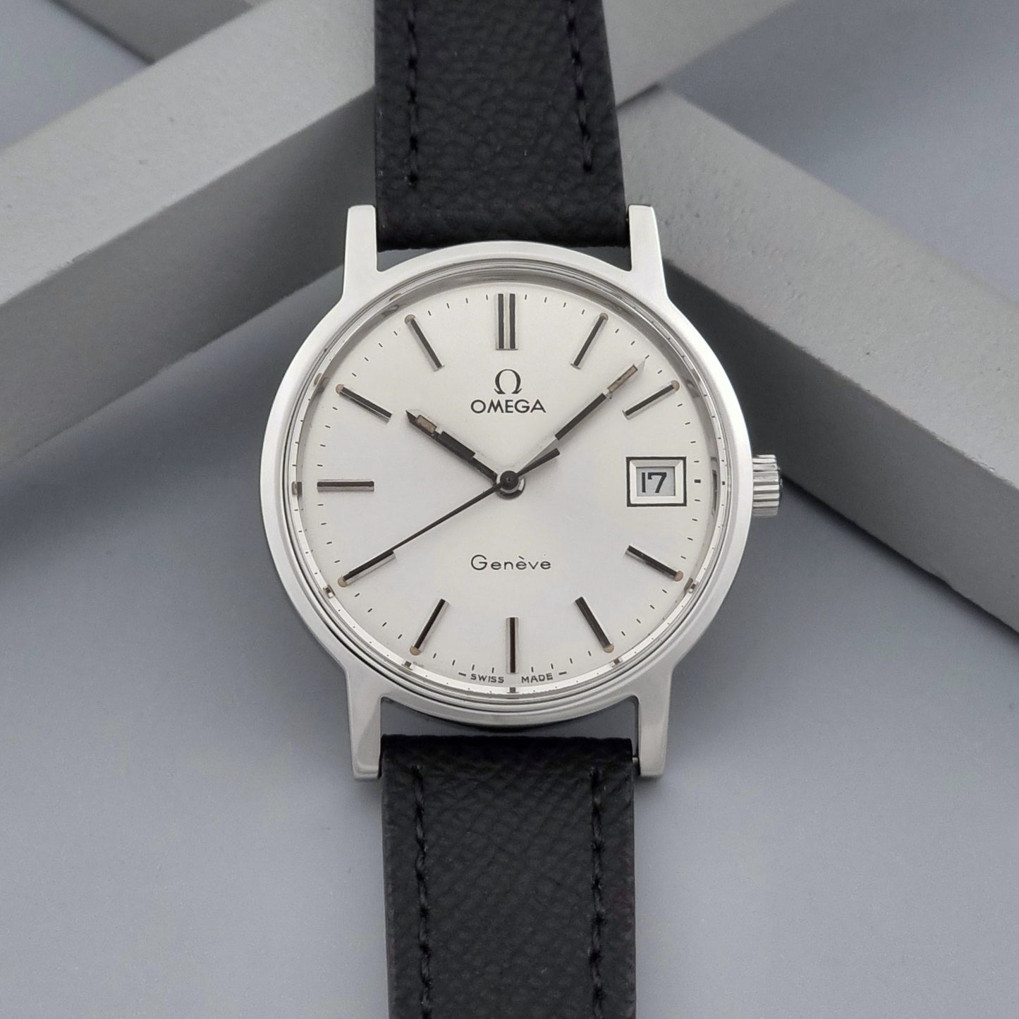 Vintage Omega Geneve 136.0098 Wristwatch with black strap and silver case on a gray background dial view