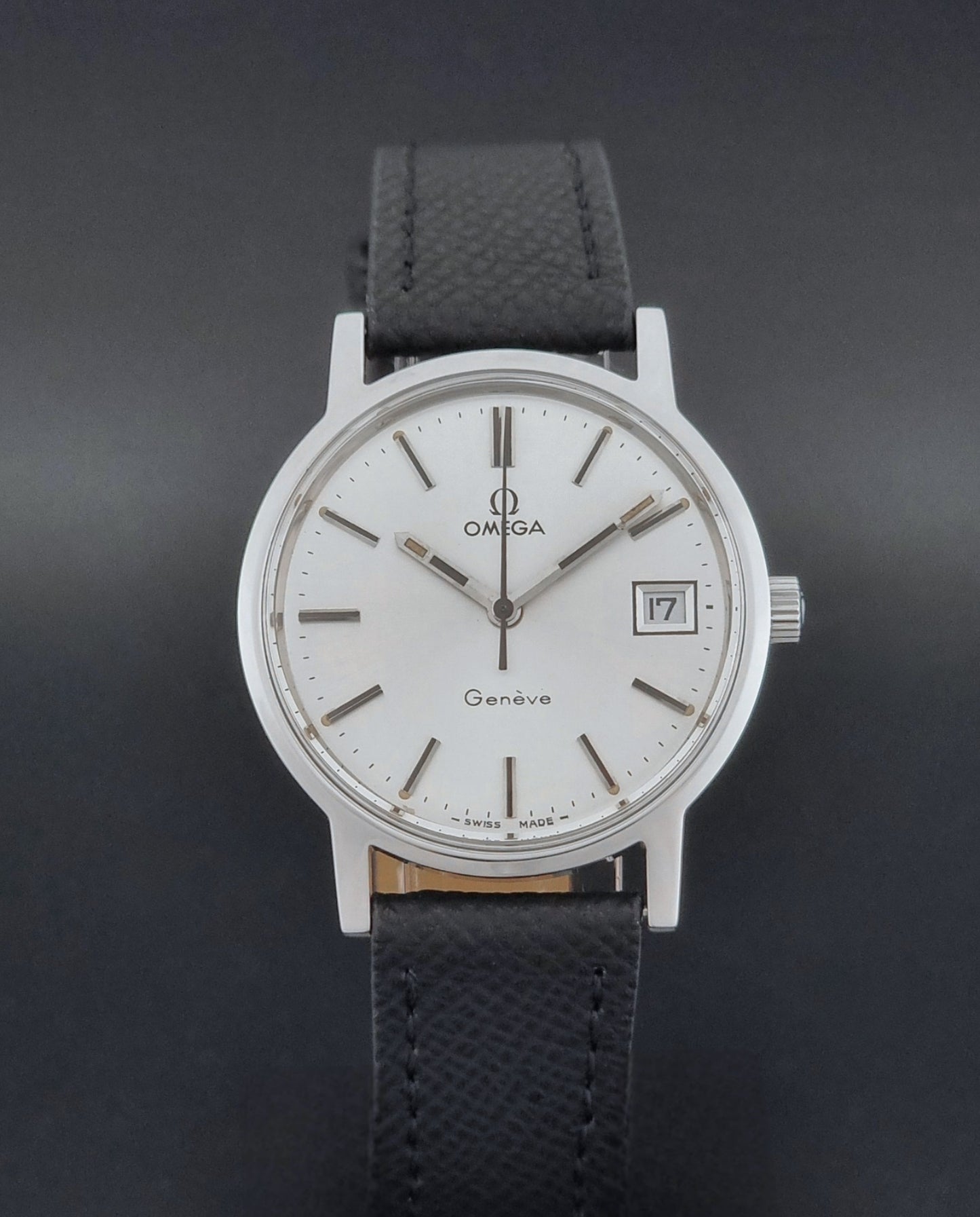 Vintage Omega Geneve 136.0098 Wristwatch with black strap and silver case on a gray background close dial view