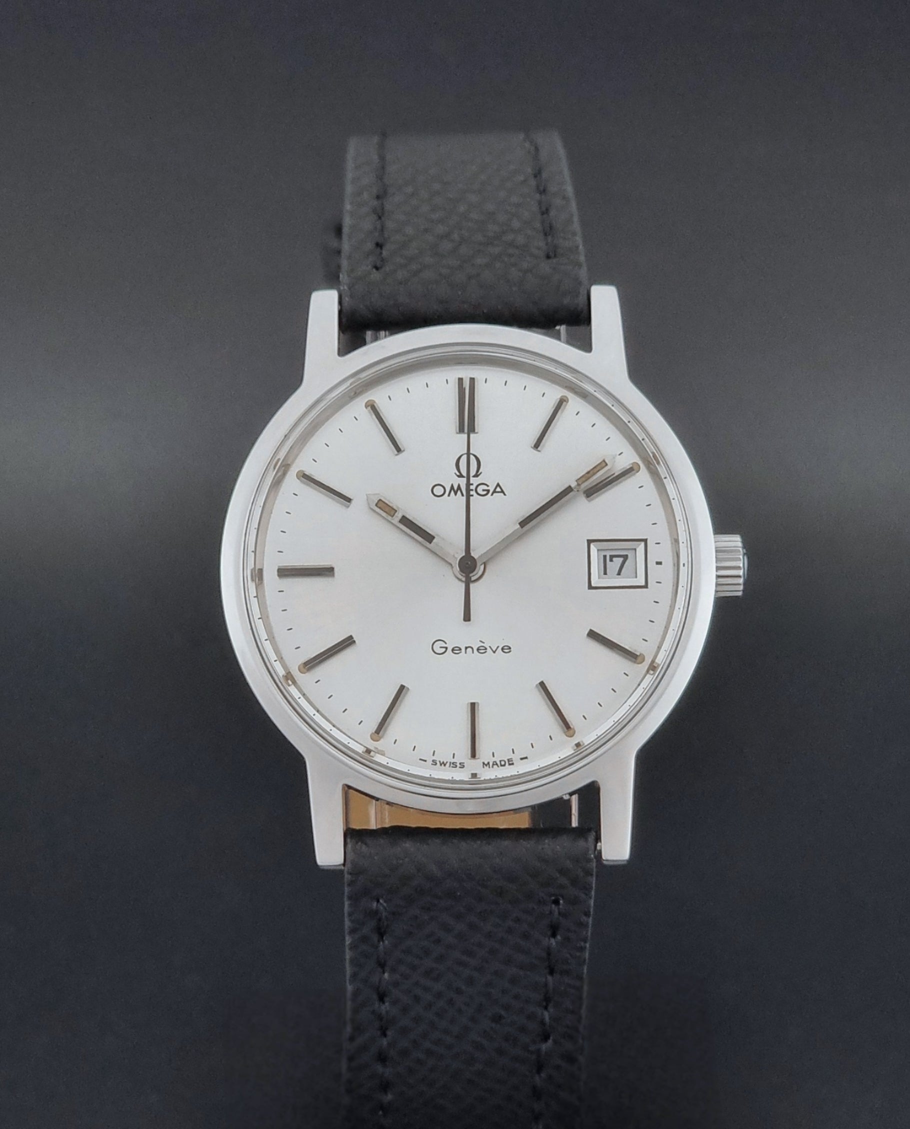 Vintage Omega Geneve 136.0098 Wristwatch with black strap and silver case on a gray background close dial view