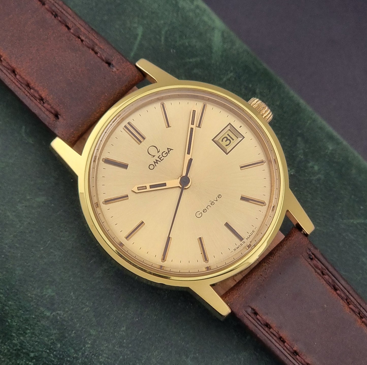 Vintage Omega Wristwatch Geneve 136.0098 with brown leather strap on a green surface close dial view