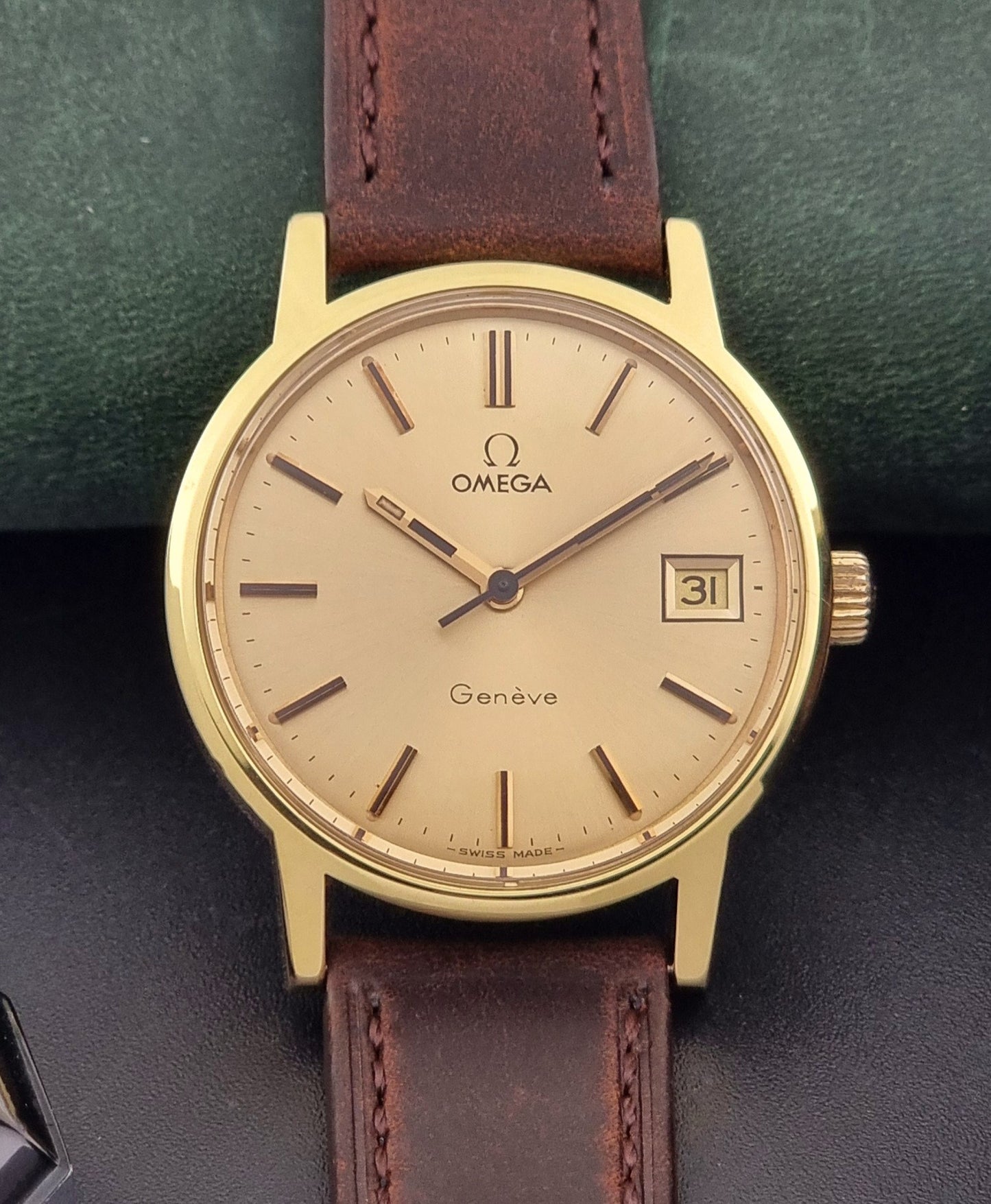 Vintage Omega Wristwatch Geneve 136.0098 with brown leather strap on a green surface close up dial view