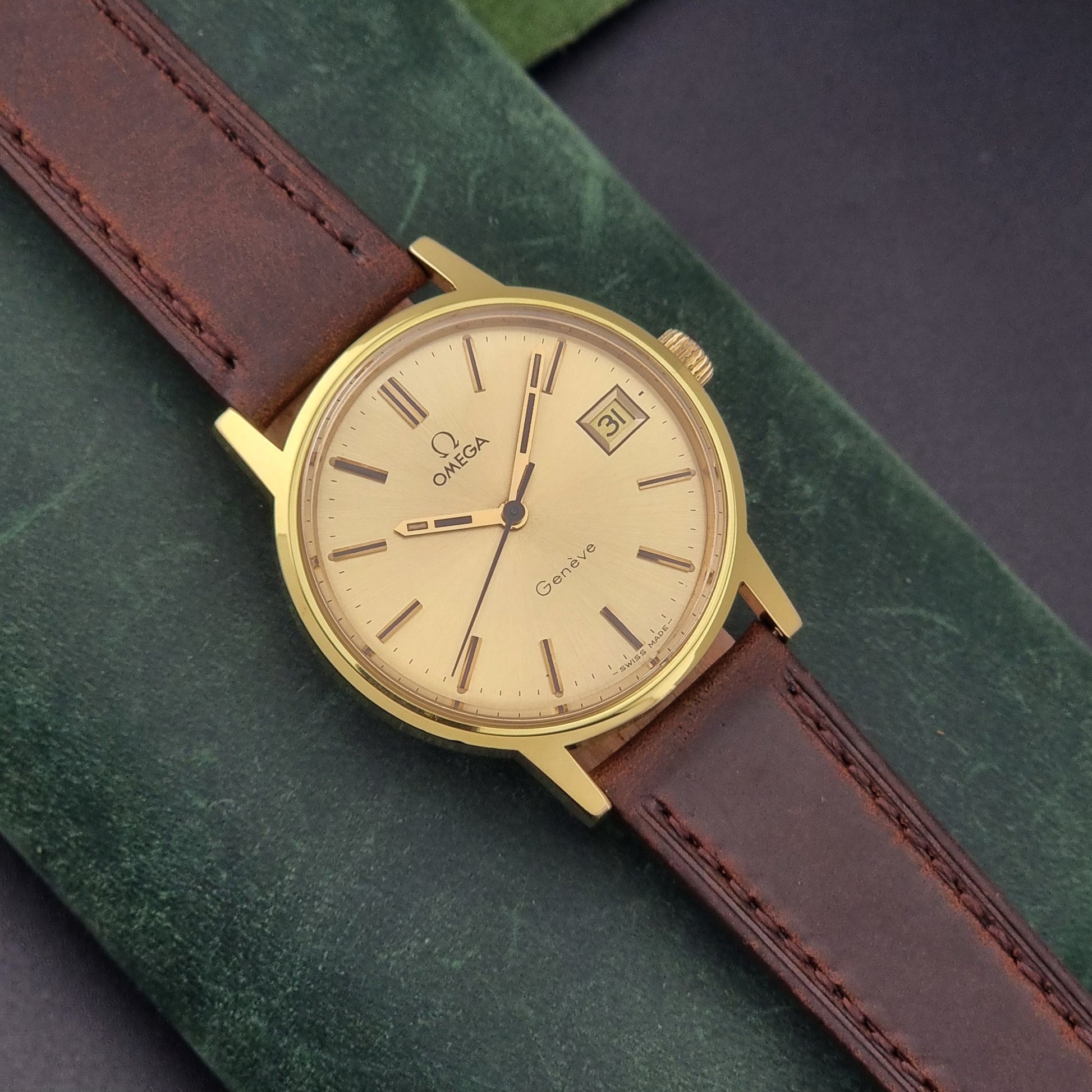 Vintage Omega Wristwatch Geneve 136.0098 with brown leather strap on a green surface front