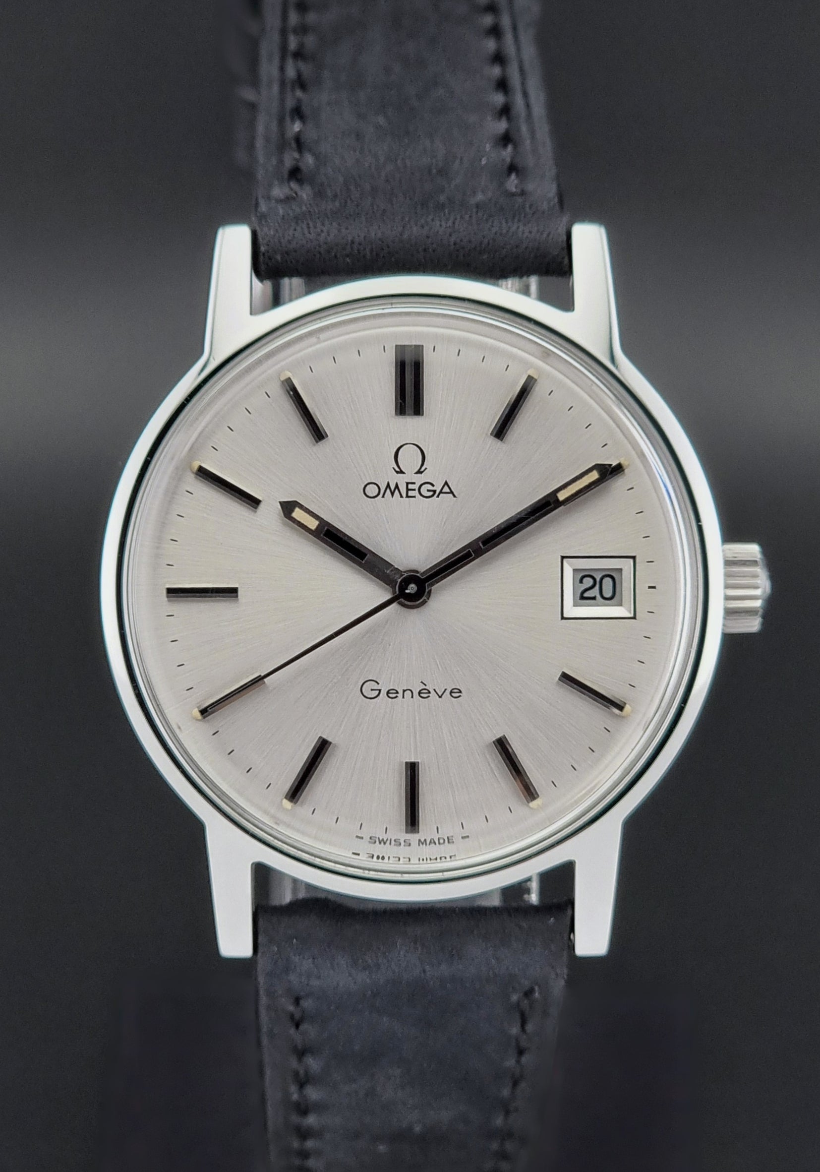 Vintage Omega Geneve watch with silver case and blue leather strap on a dark background