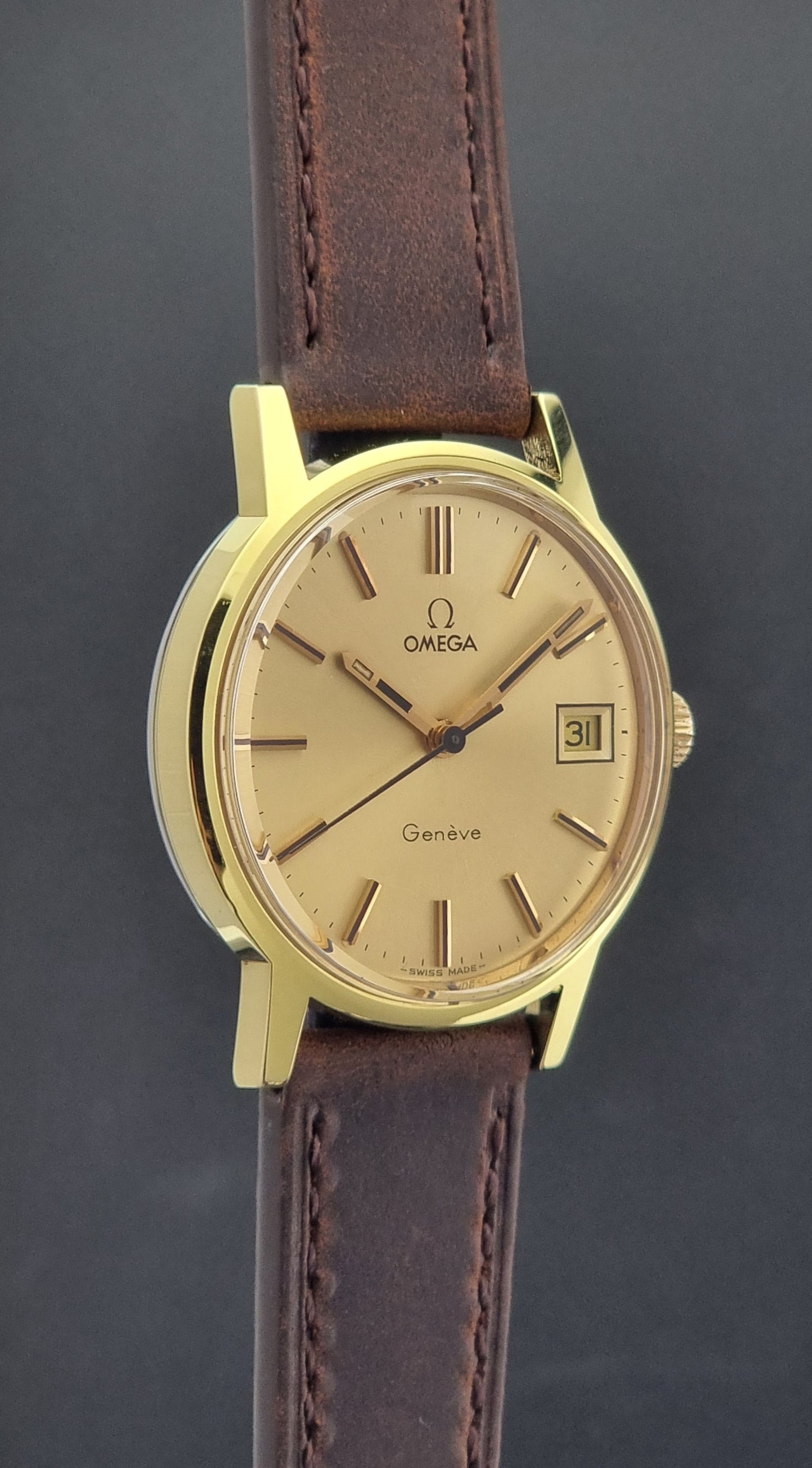 Vintage Omega Wristwatch Geneve 136.0098 with brown leather strap on a green surface side profile view