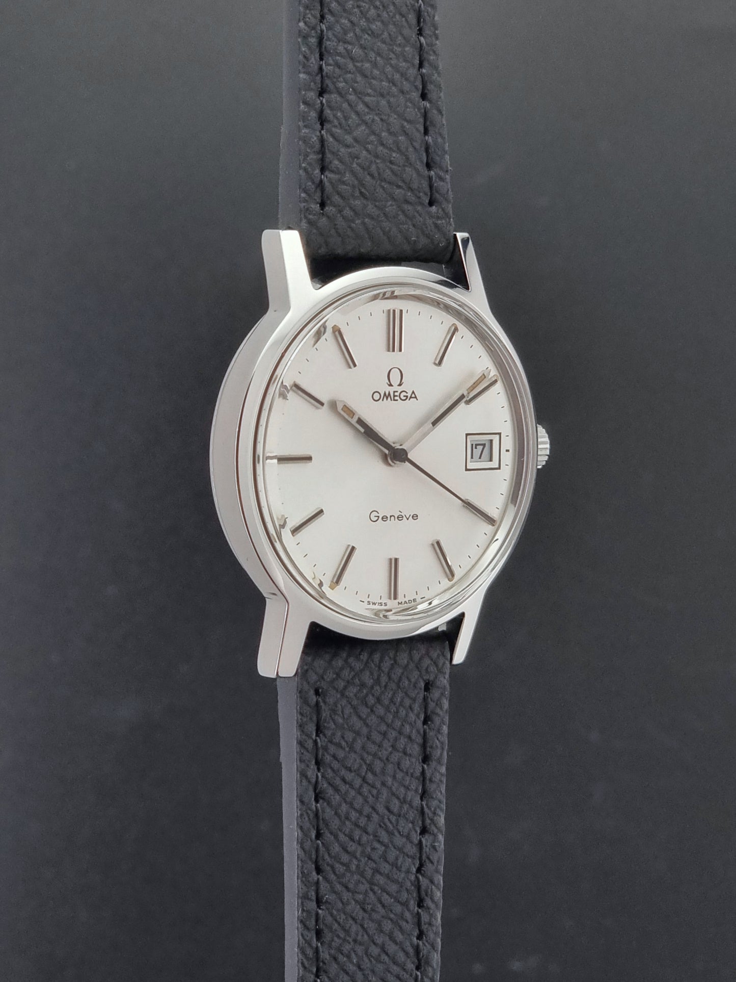 Vintage Omega Geneve 136.0098 Wristwatch with black strap and silver case on a gray background side profile view