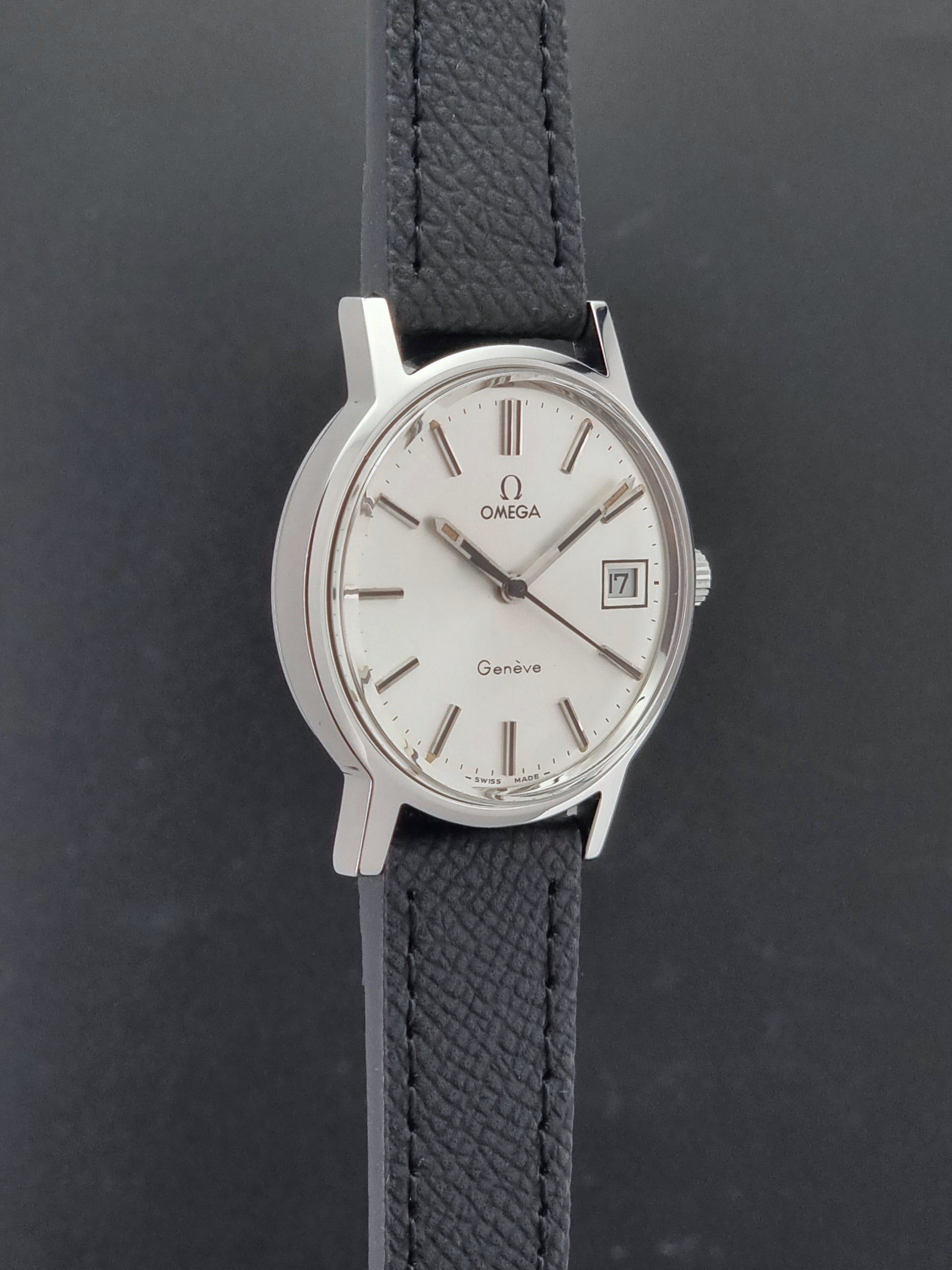 Vintage Omega Geneve 136.0098 Wristwatch with black strap and silver case on a gray background side profile view