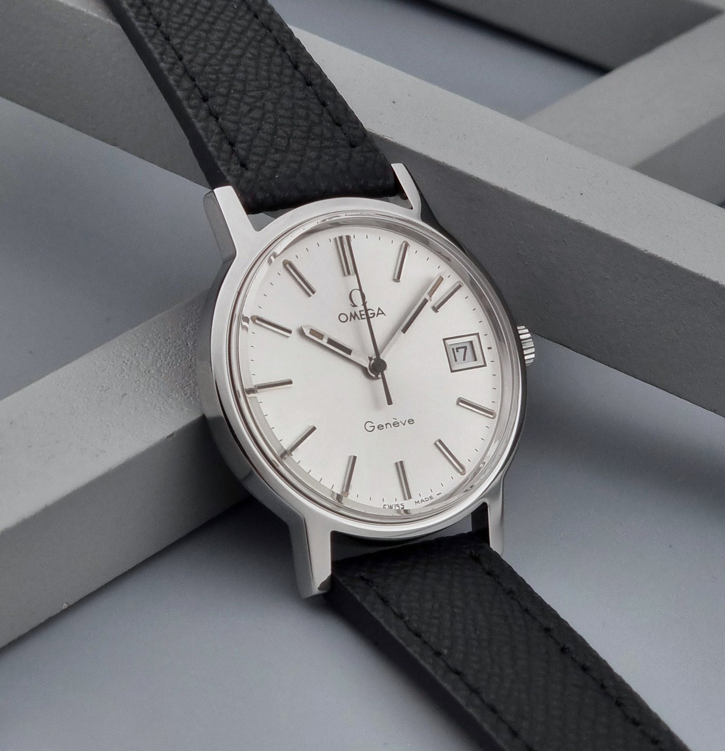 Vintage Omega Geneve 136.0098 Wristwatch with black strap and silver case on a gray background side view