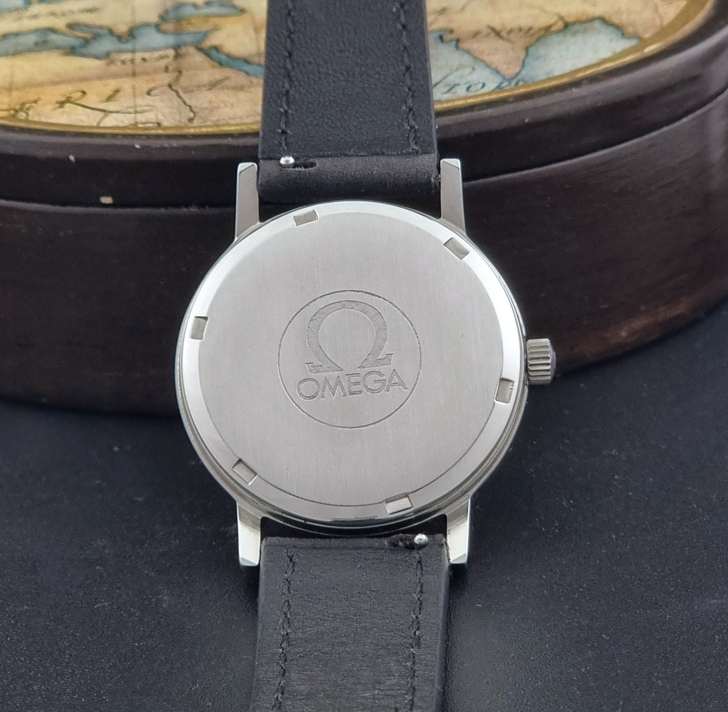Vintage Omega Wristwatch Geneve 136.0099 with a black leather strap on a dark surface case back view