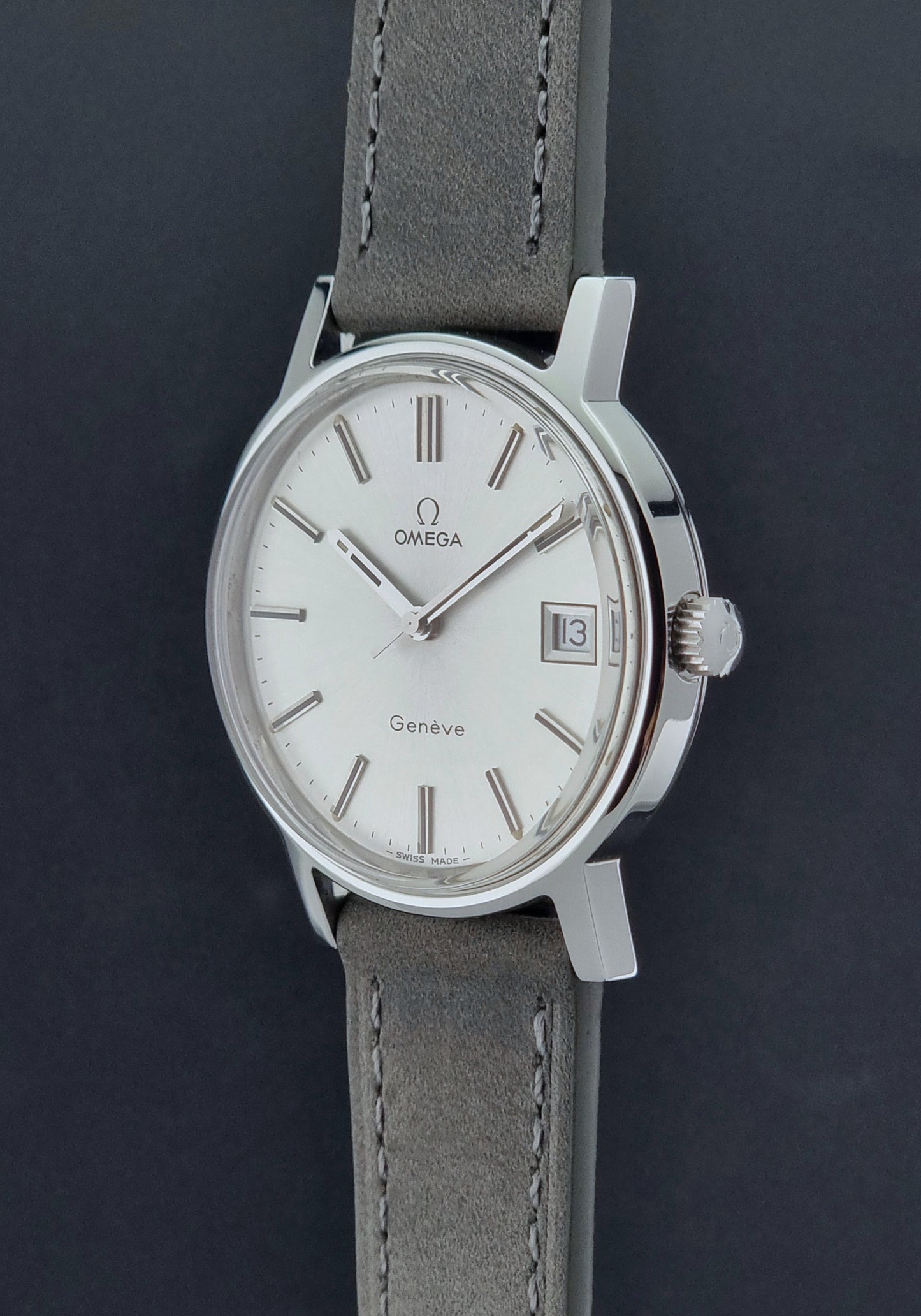 Vintage Omega Wristwatch Geneve 136.0099 with a grey leather strap on a grey background crown profile view