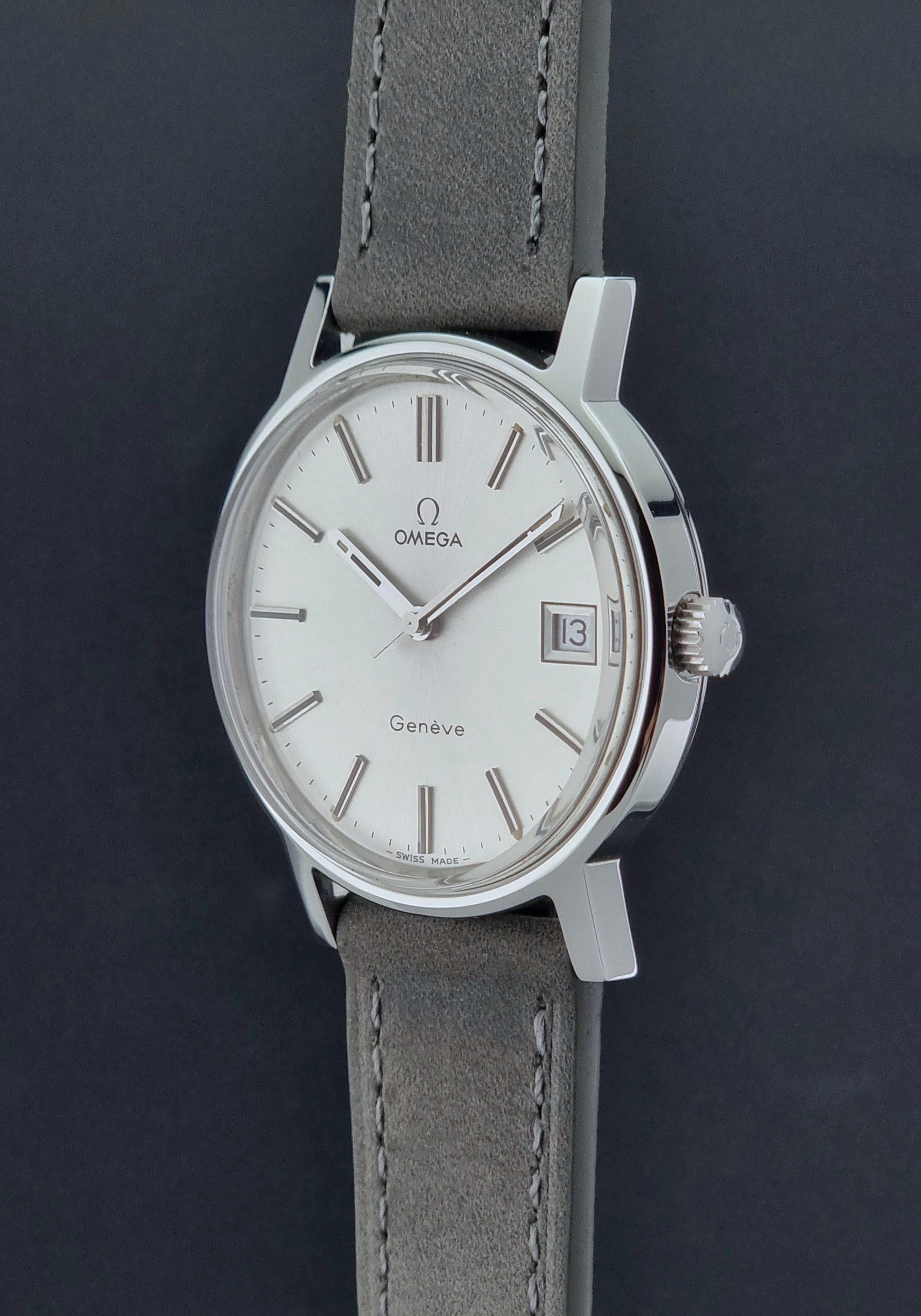 Vintage Omega Wristwatch Geneve 136.0099 with a grey leather strap on a grey background crown profile view