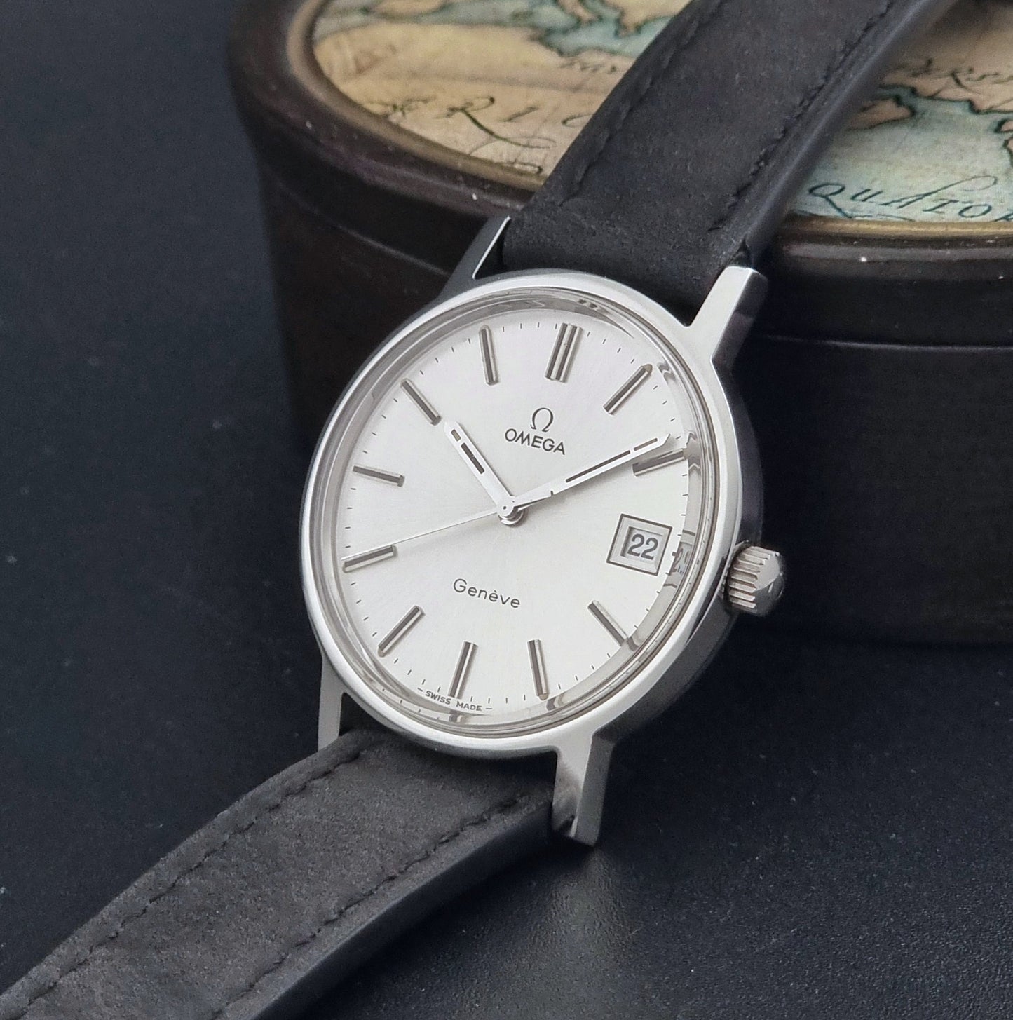 Vintage Omega Wristwatch Geneve 136.0099 with a black leather strap on a dark surface crown view