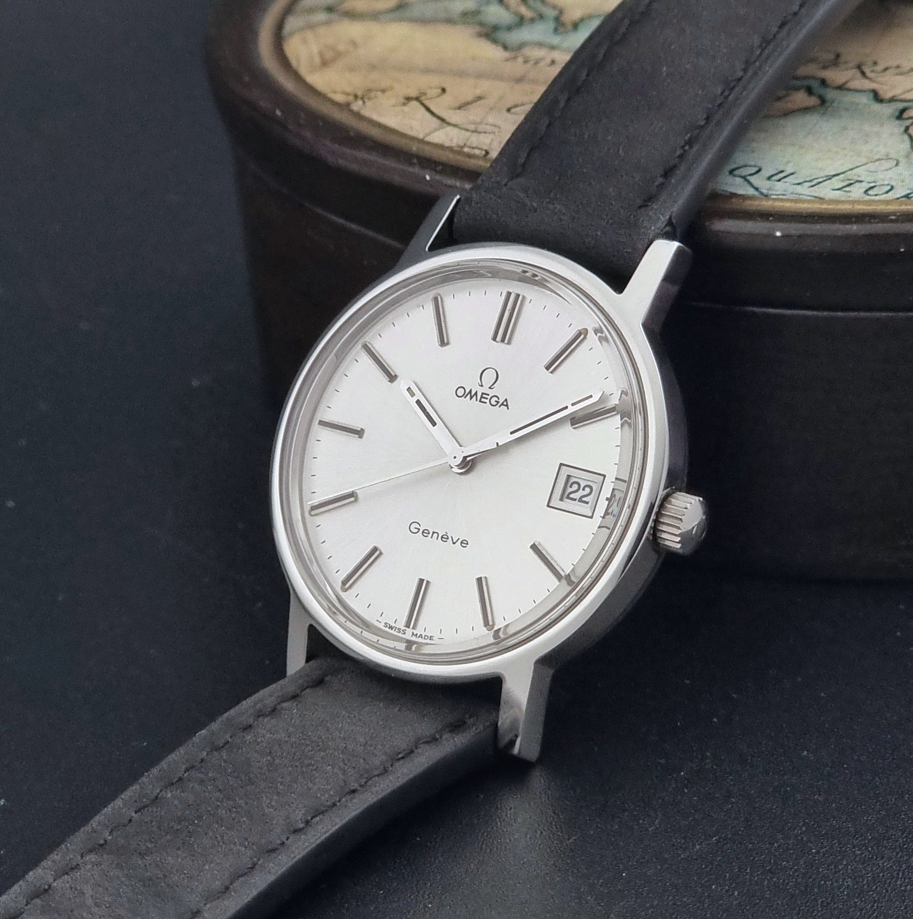 Vintage Omega Wristwatch Geneve 136.0099 with a black leather strap on a dark surface crown view