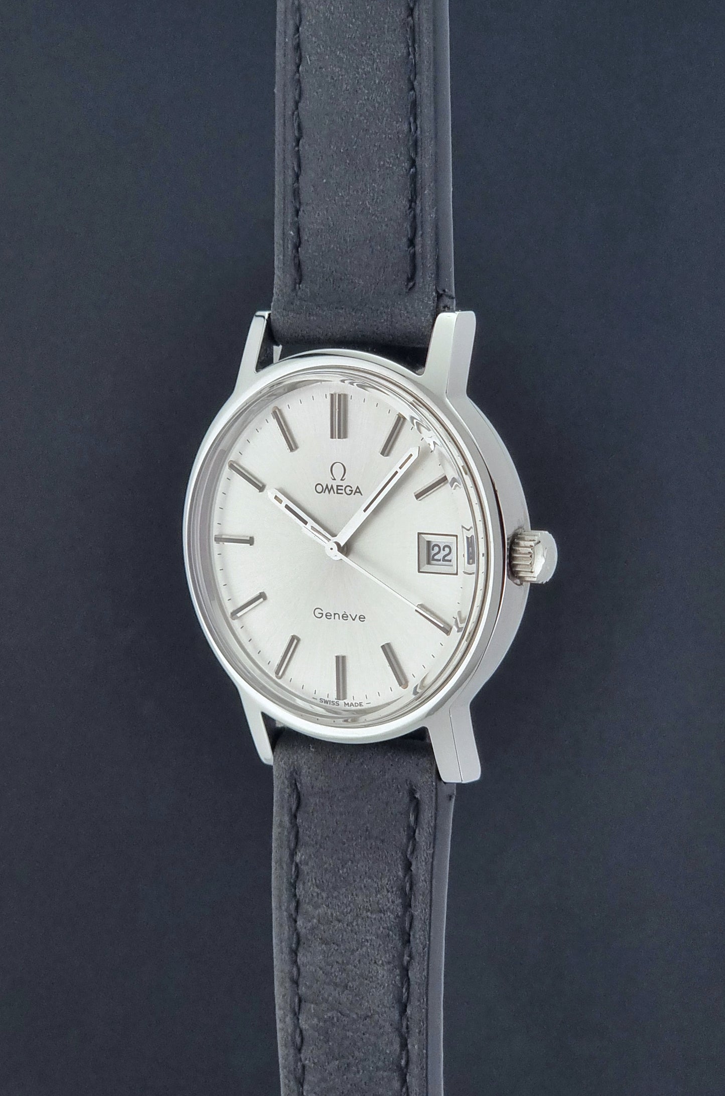 Vintage Omega Wristwatch Geneve 136.0099 with a black leather strap on a dark surface crown profile view
