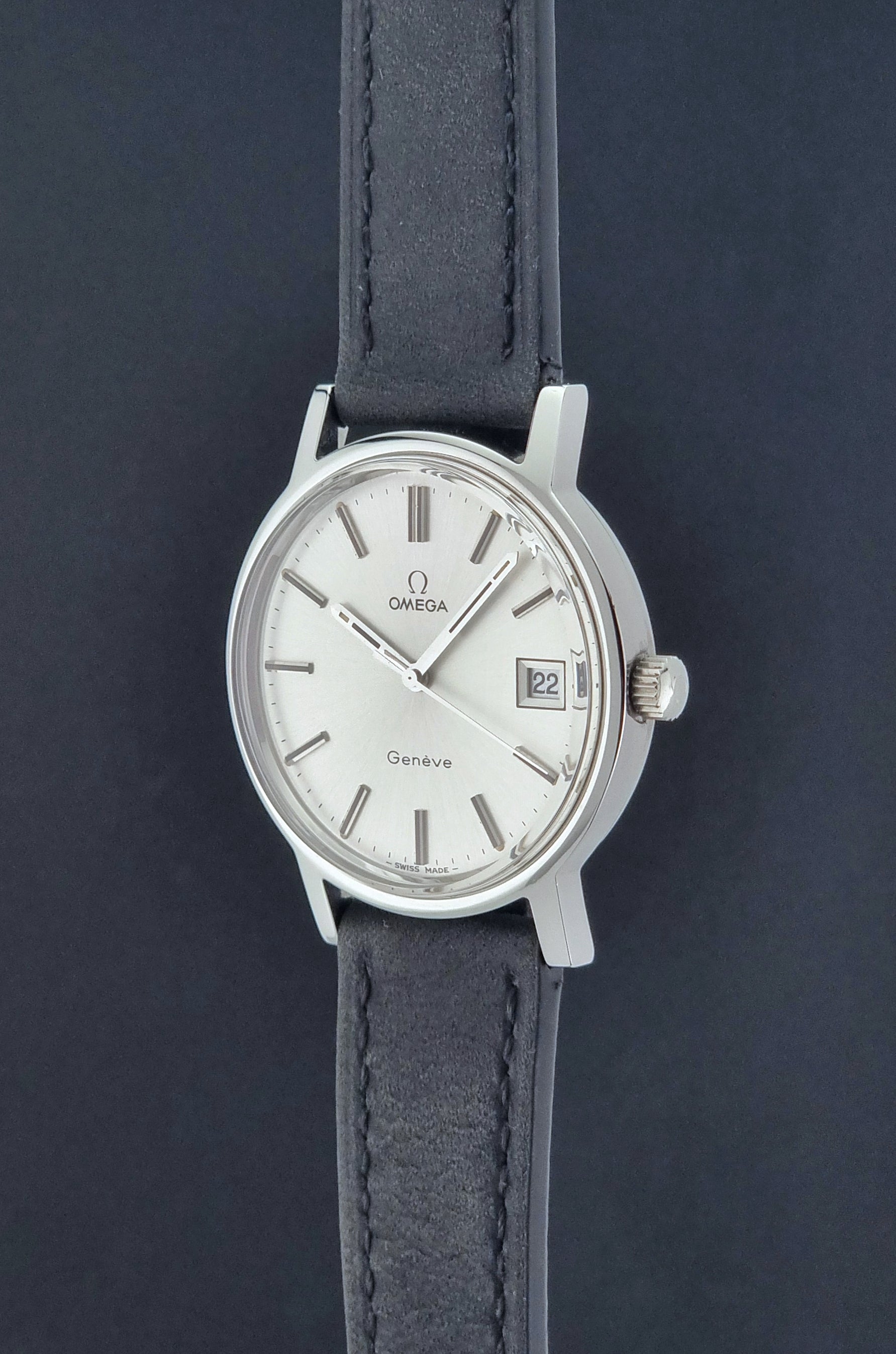 Vintage Omega Wristwatch Geneve 136.0099 with a black leather strap on a dark surface crown profile view