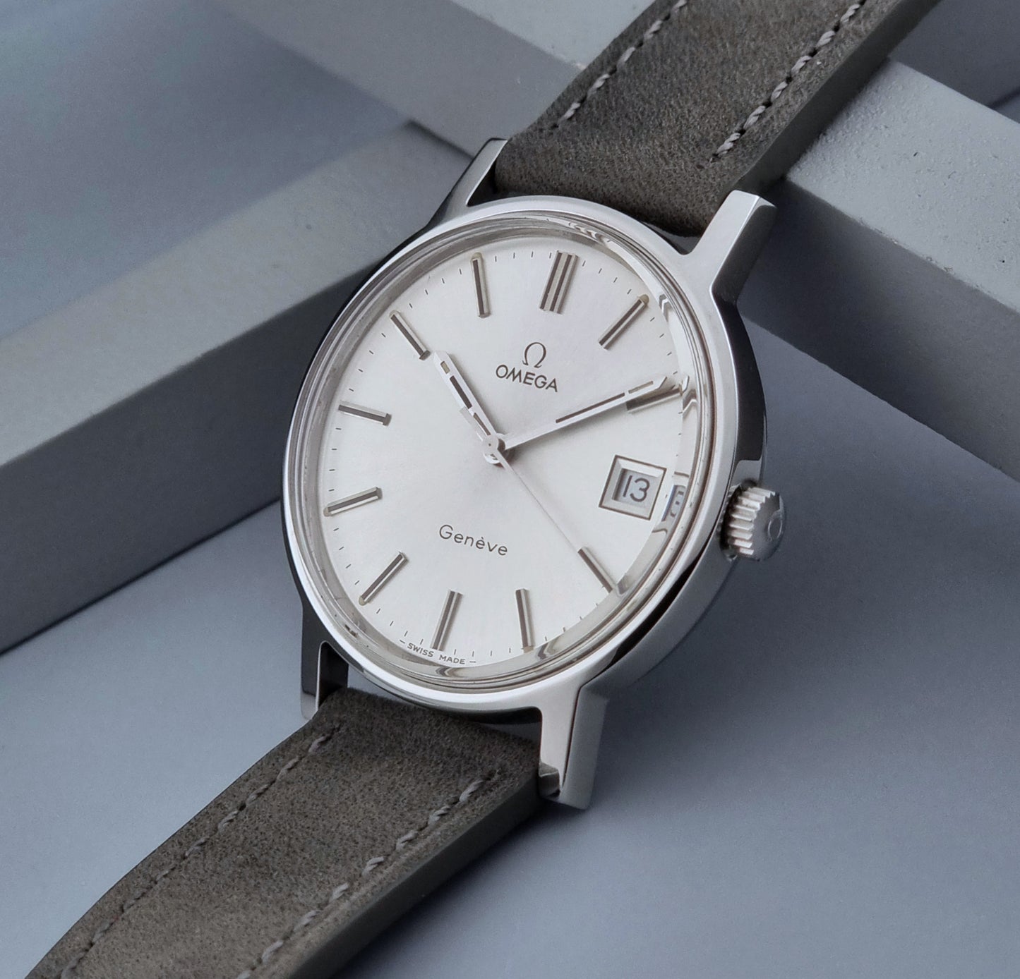 Vintage Omega Wristwatch Geneve 136.0099 with a grey leather strap on a grey background crown view