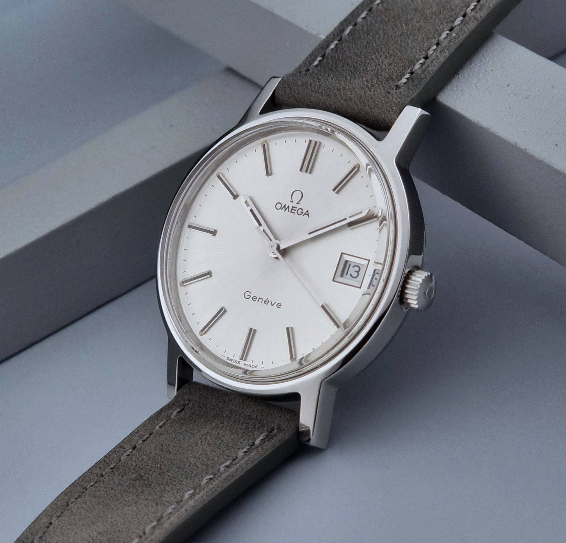 Vintage Omega Wristwatch Geneve 136.0099 with a grey leather strap on a grey background crown view